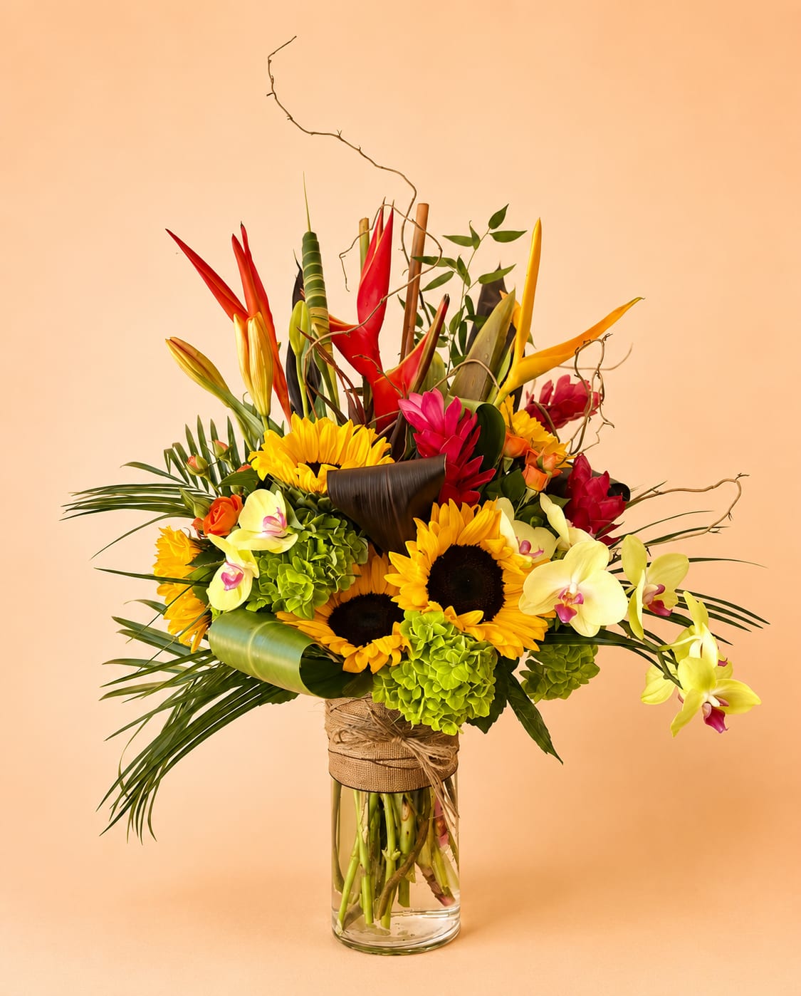 Tropical bouquet with sunflowers, orchids, and red heliconia in a glass vase