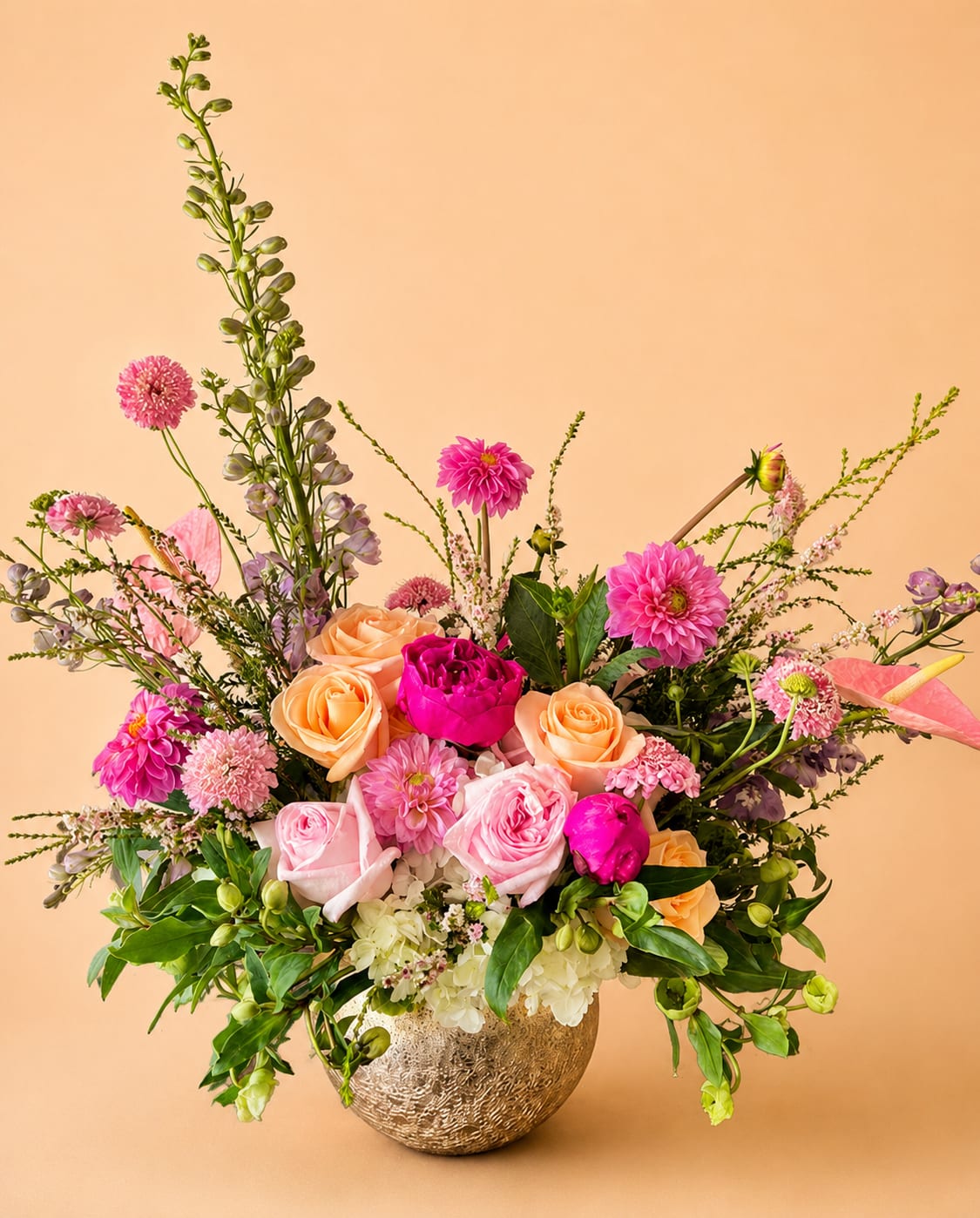 Enchant Me - Our “Enchant Me” arrangement inspires fresh blush beauty surrounded by gardenful greenery and blooms. Florals included in this arrangement are hydrangeas, hellebores, fragrant pink garden roses, dahlias, peonies, scabiosas, lavender delphinium, tiffany roses, pink anthuriums, and whimsical spirea. Arranged in a gold round fishbowl style vase. 