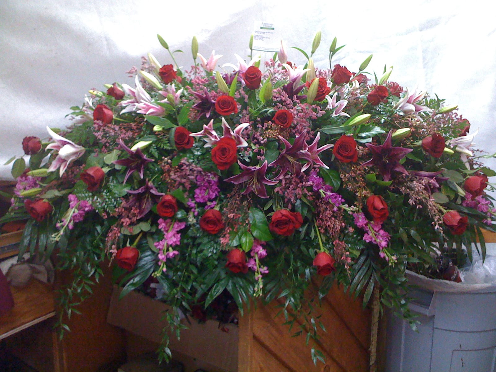 Large casket spray with red roses, lilies, and pink filler flowers