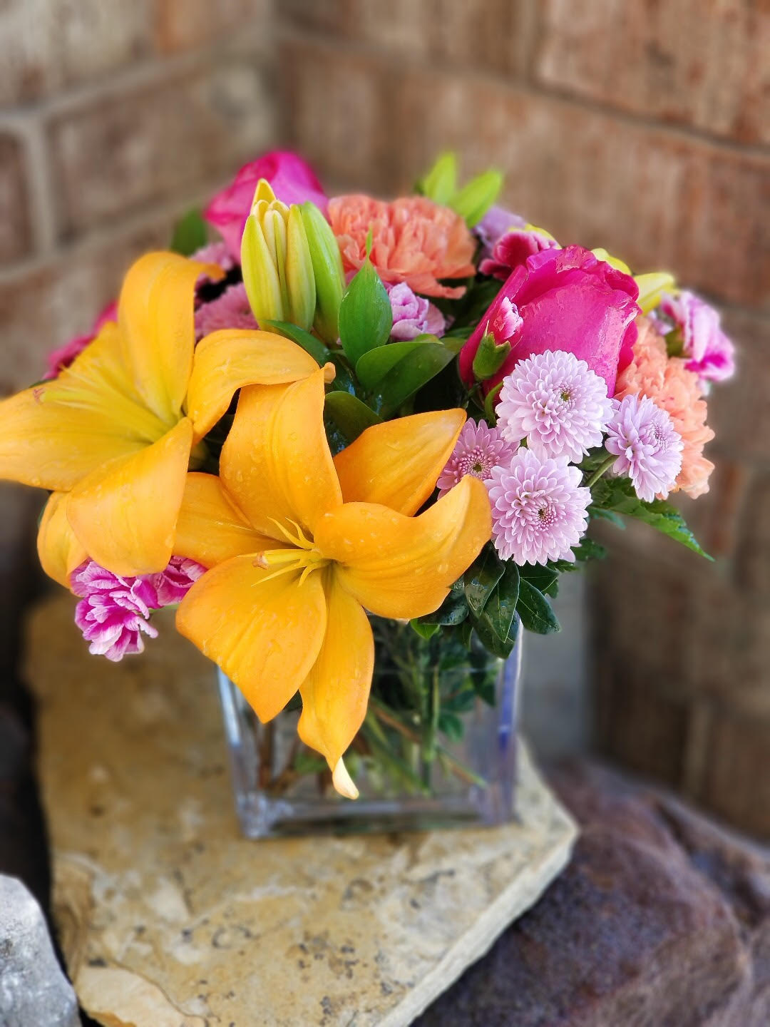 Colorful bouquet with yellow lilies, pink roses, and lavender mums in a glass vase