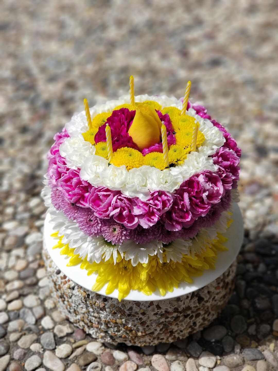 Round floral cake with pink, white, and yellow flowers and candles