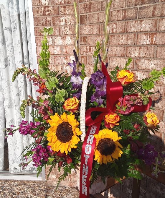 Standing floral spray with sunflowers, roses, and purple blooms on a ribboned easel