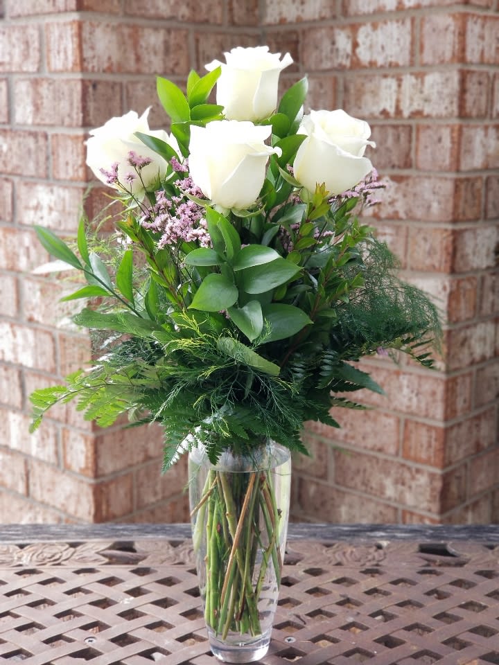 White roses arranged in a clear glass vase with greenery