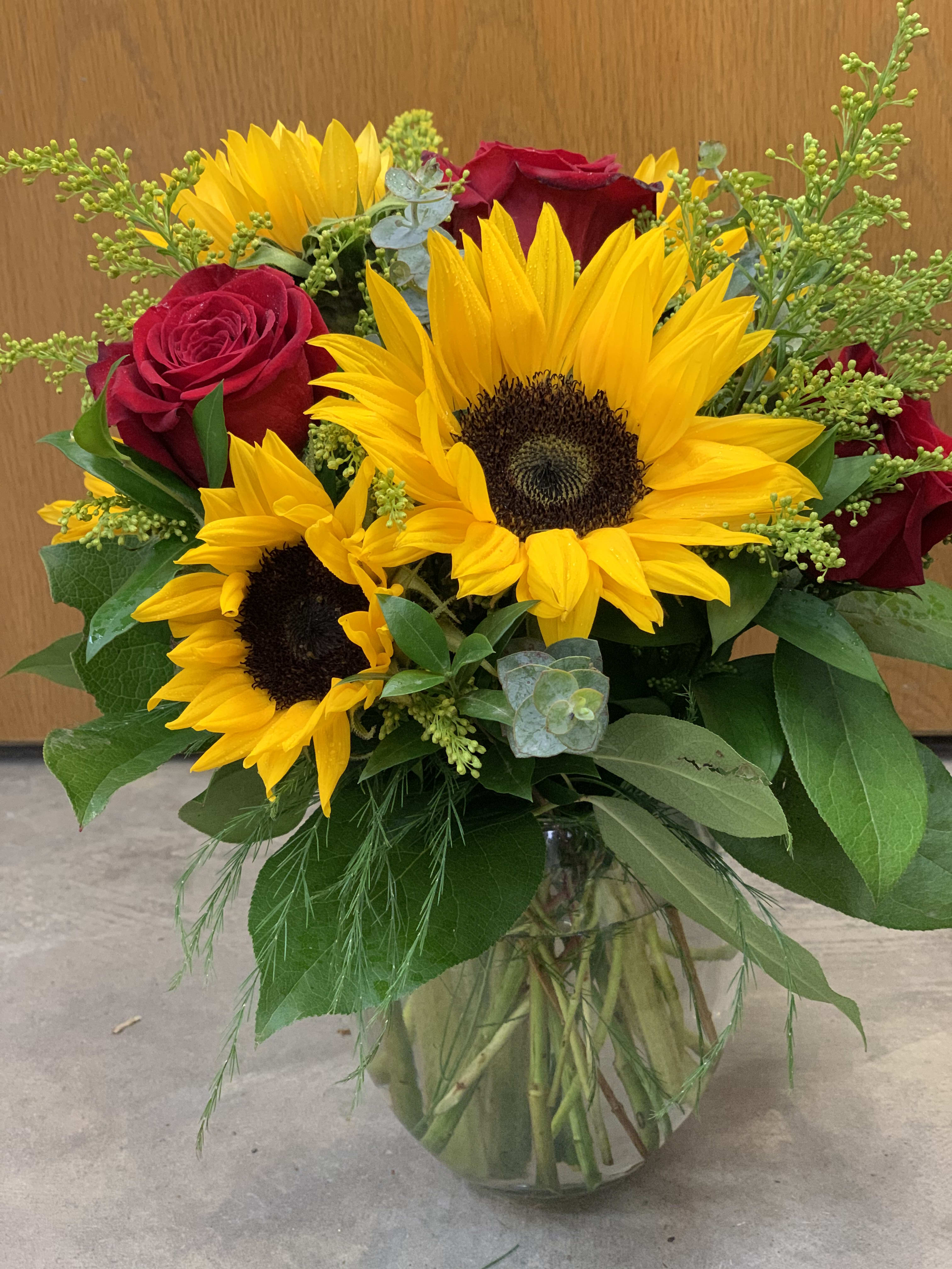 Bouquet of sunflowers and red roses in a glass vase