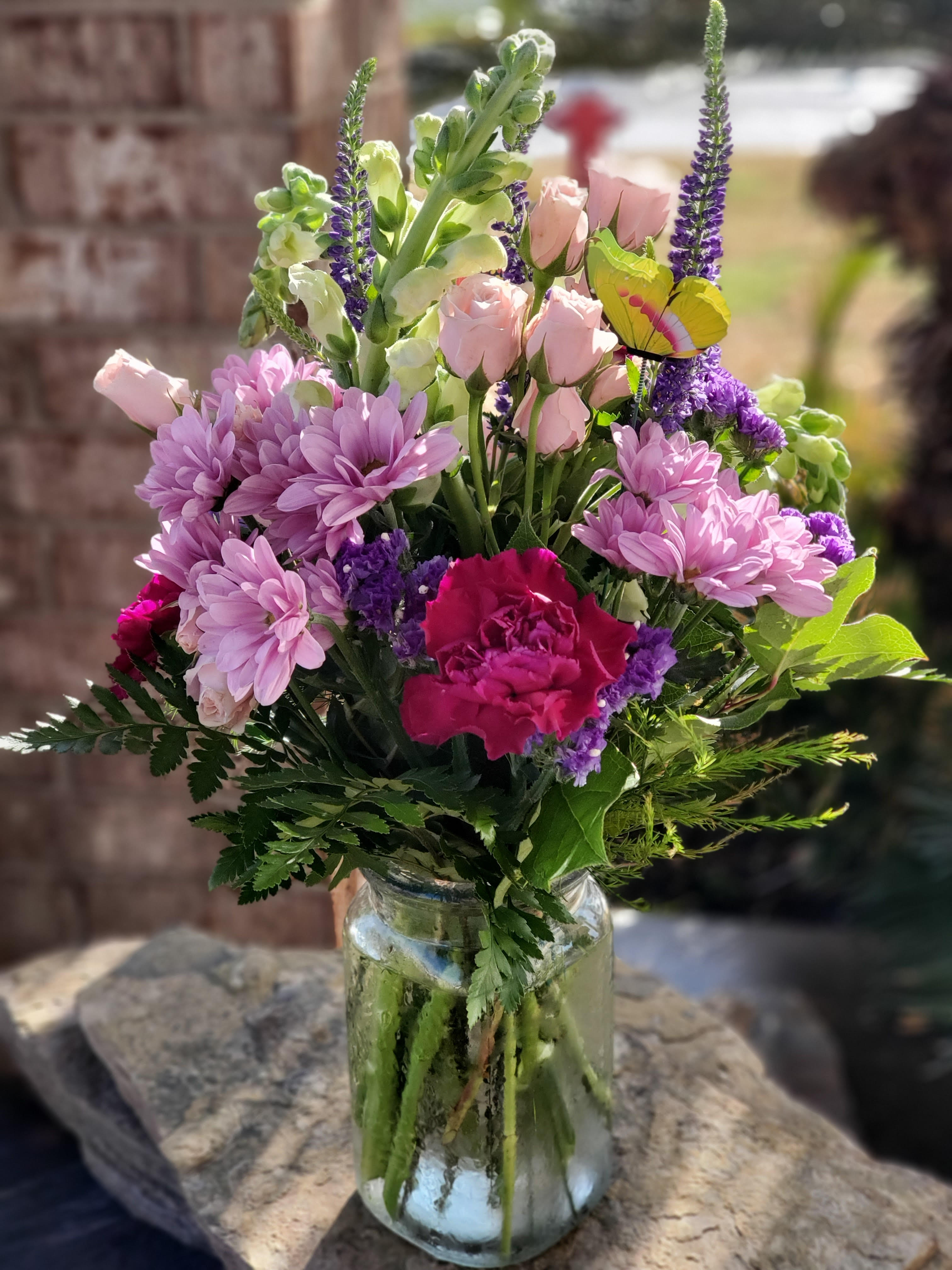 Mixed pink and purple flowers in a clear glass vase with a butterfly pick