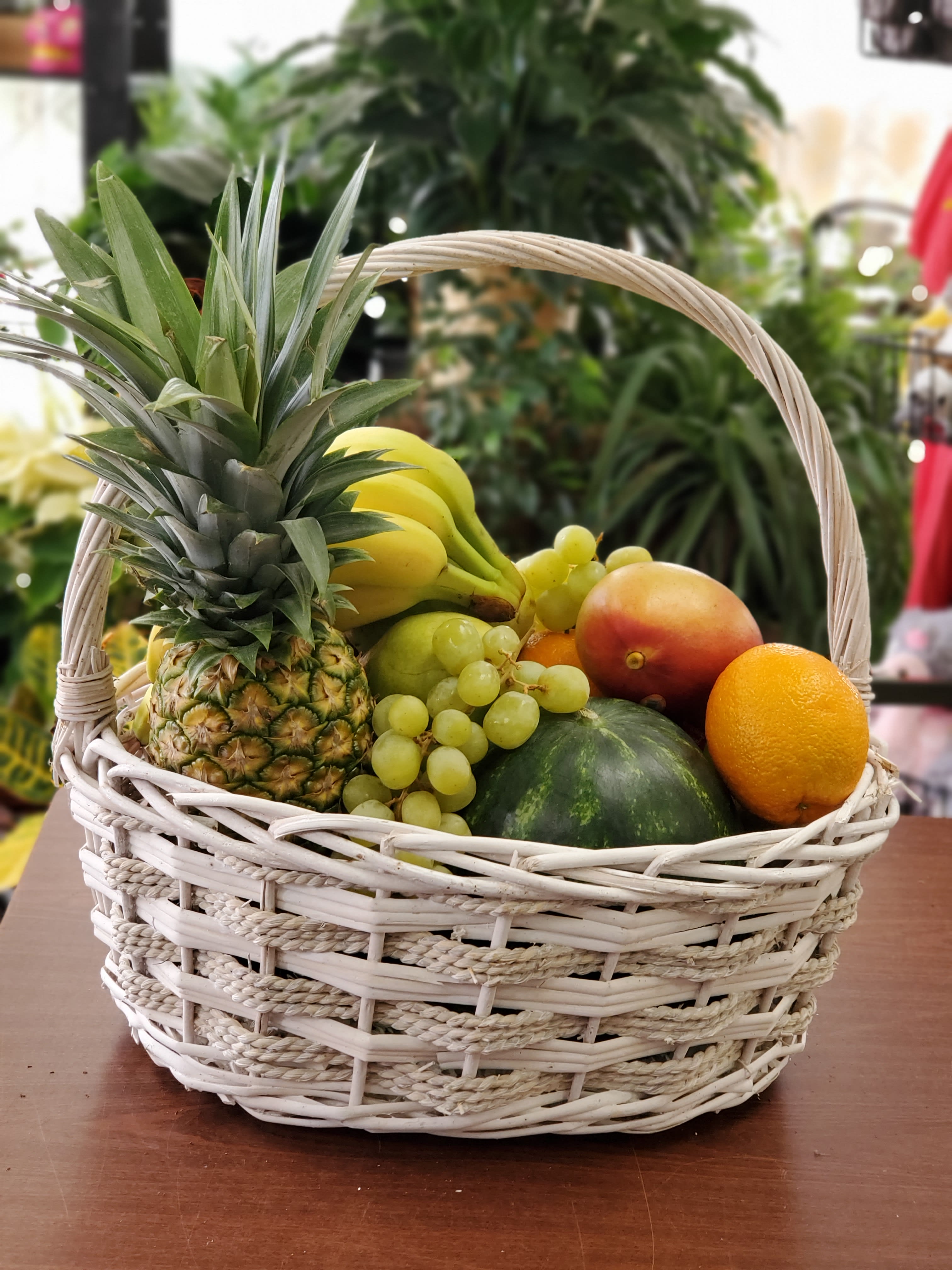 Wicker basket filled with assorted fruit including pineapple, bananas, grapes, and melon