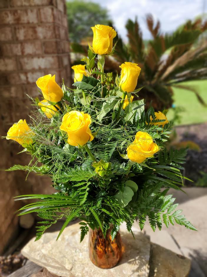 Yellow roses arranged in a glass vase with fern foliage