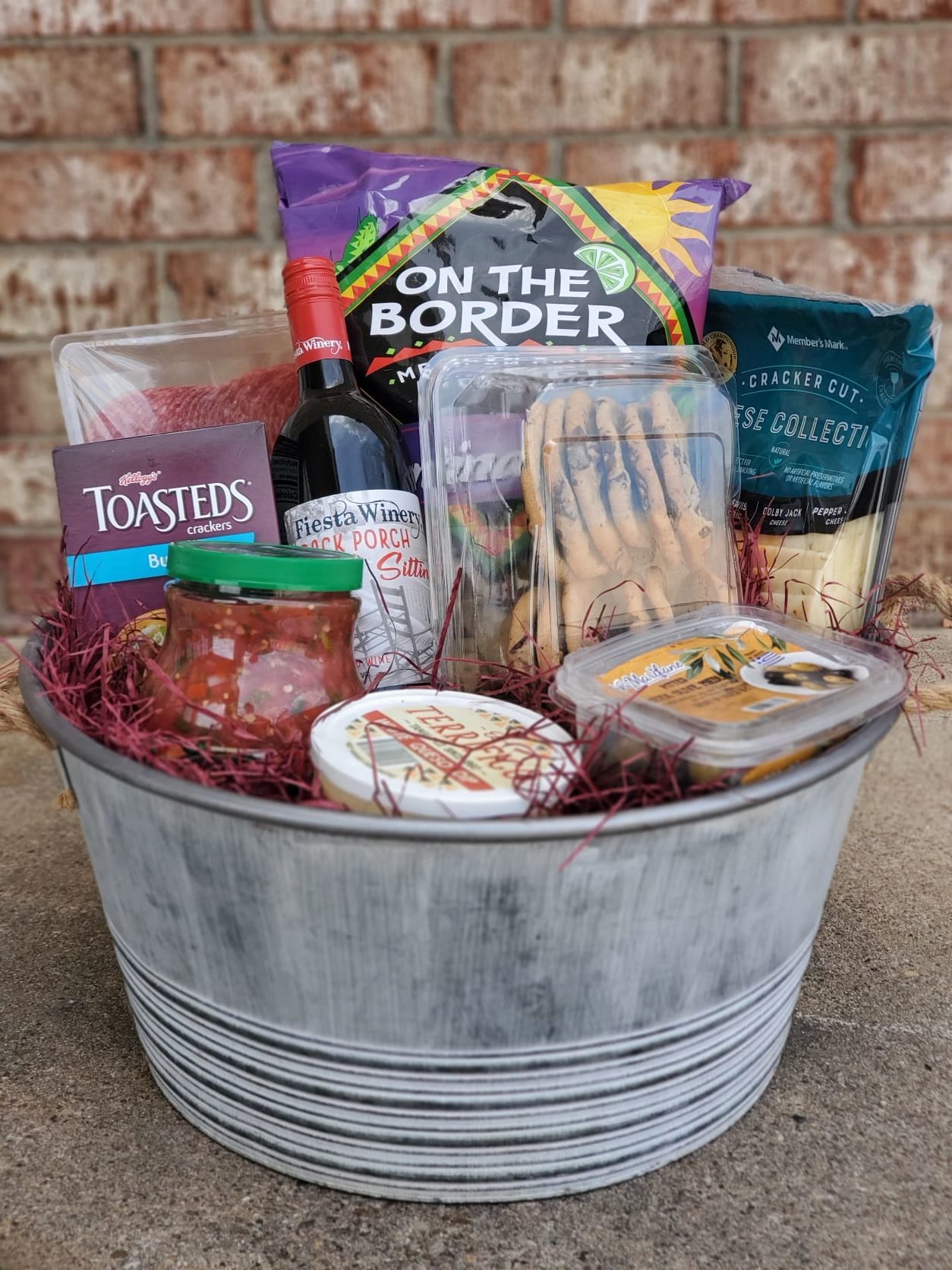 Gift basket with wine, crackers, chips, dip, and snacks in a metal tub