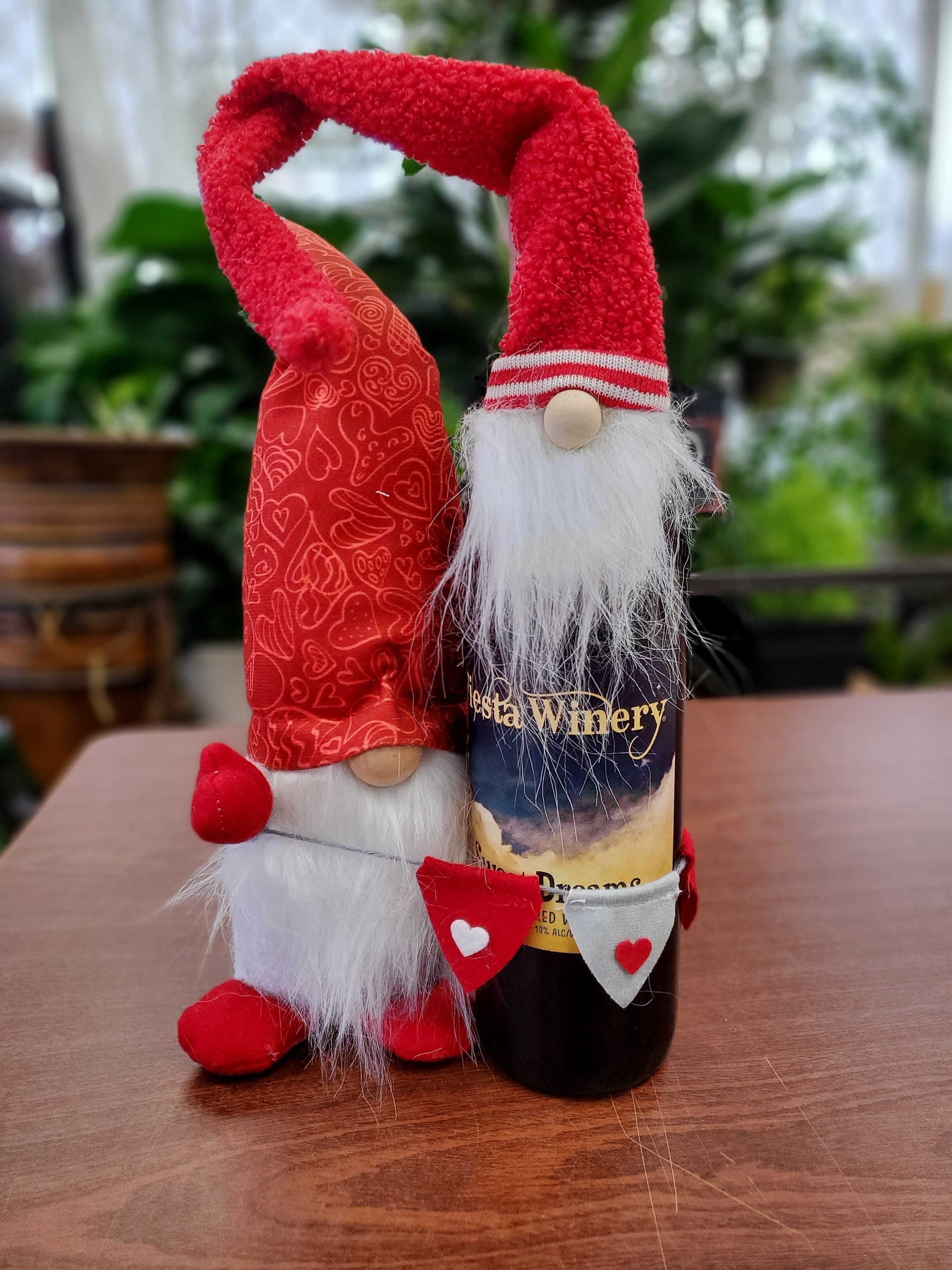 Two red gnome figurines stand beside a wine bottle on a table.