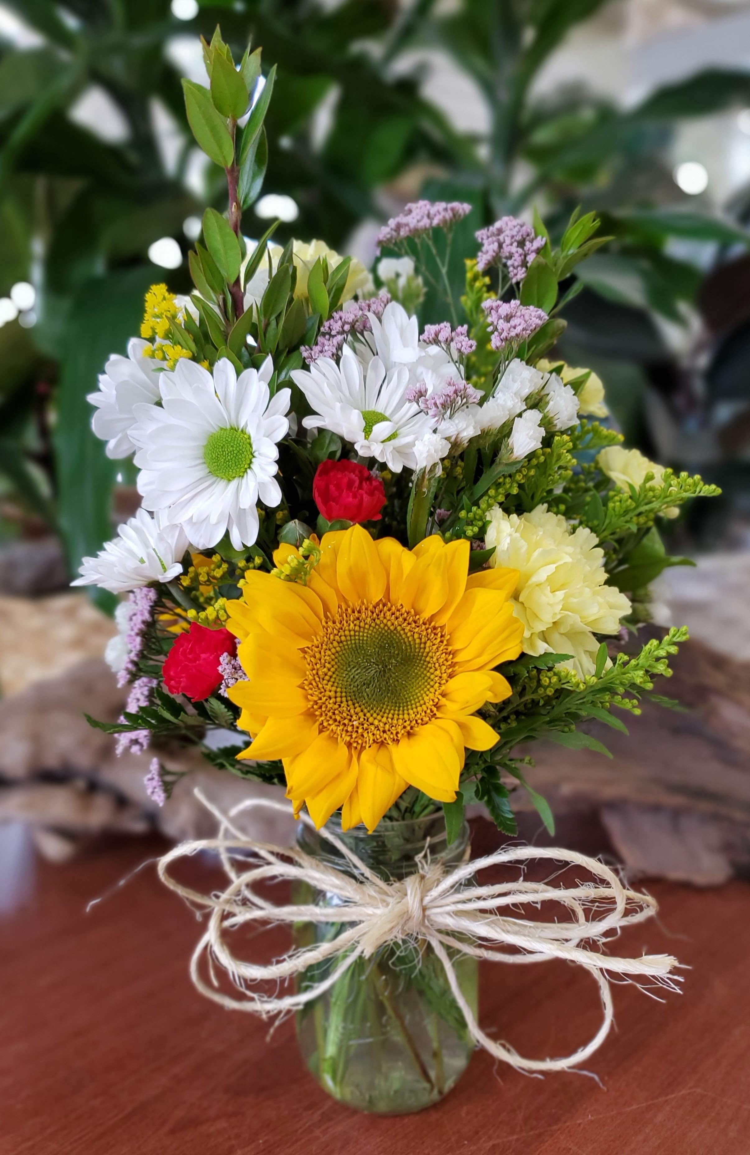 Bouquet with a sunflower, white daisies, and red carnations in a glass vase