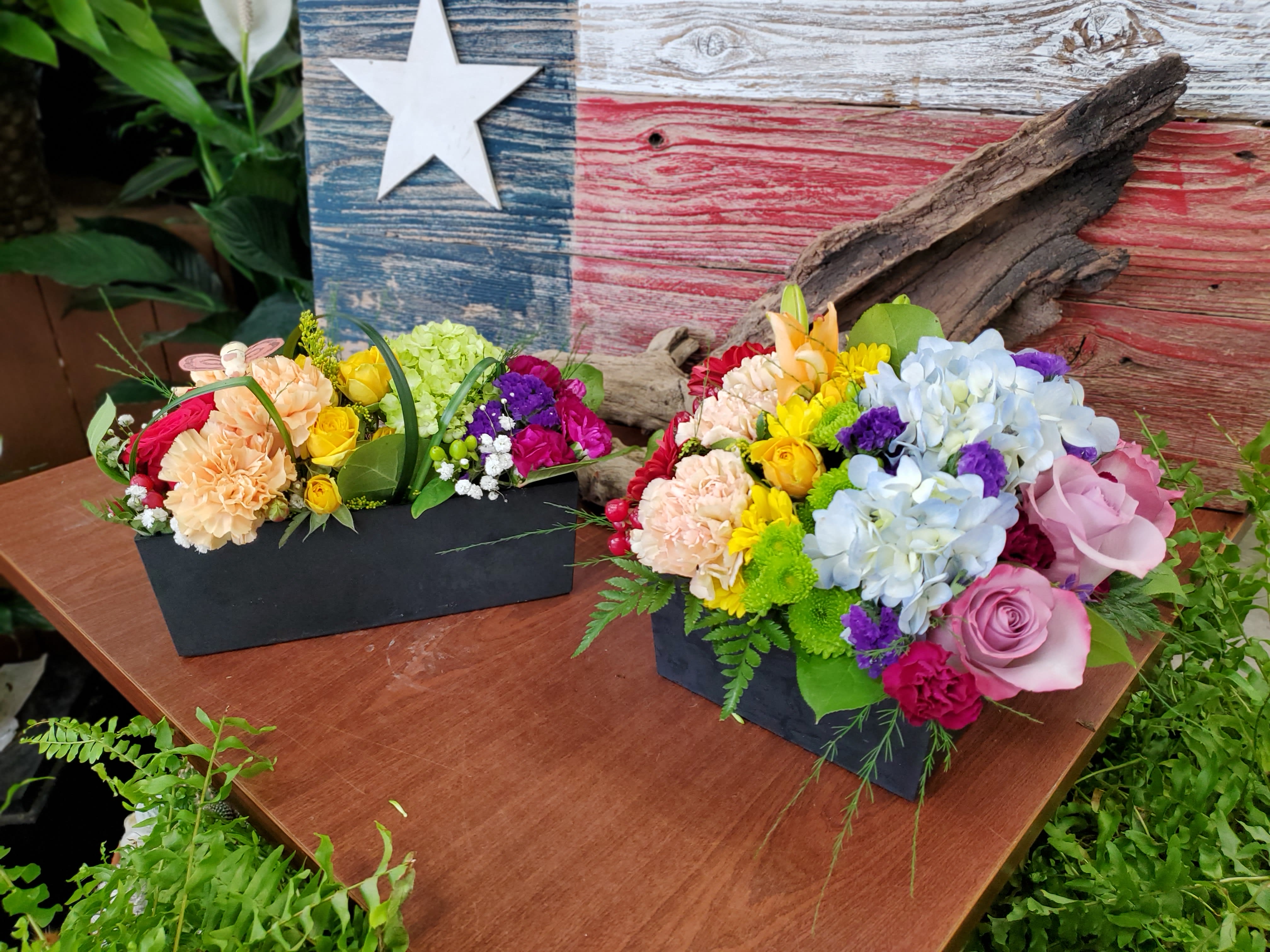 Two colorful floral arrangements in black boxes on a wooden table