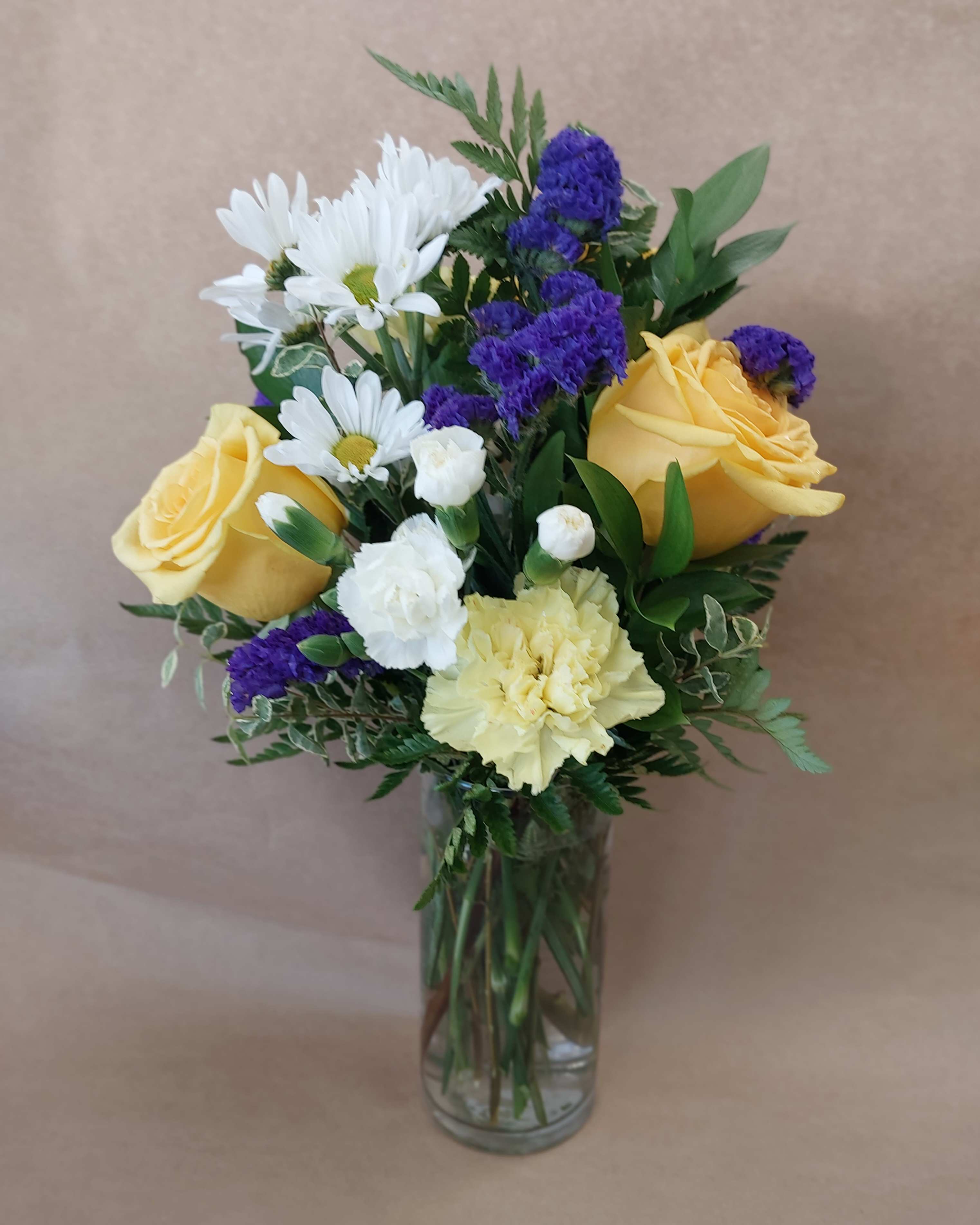 Bouquet of yellow roses, white daisies, and purple filler in a glass vase