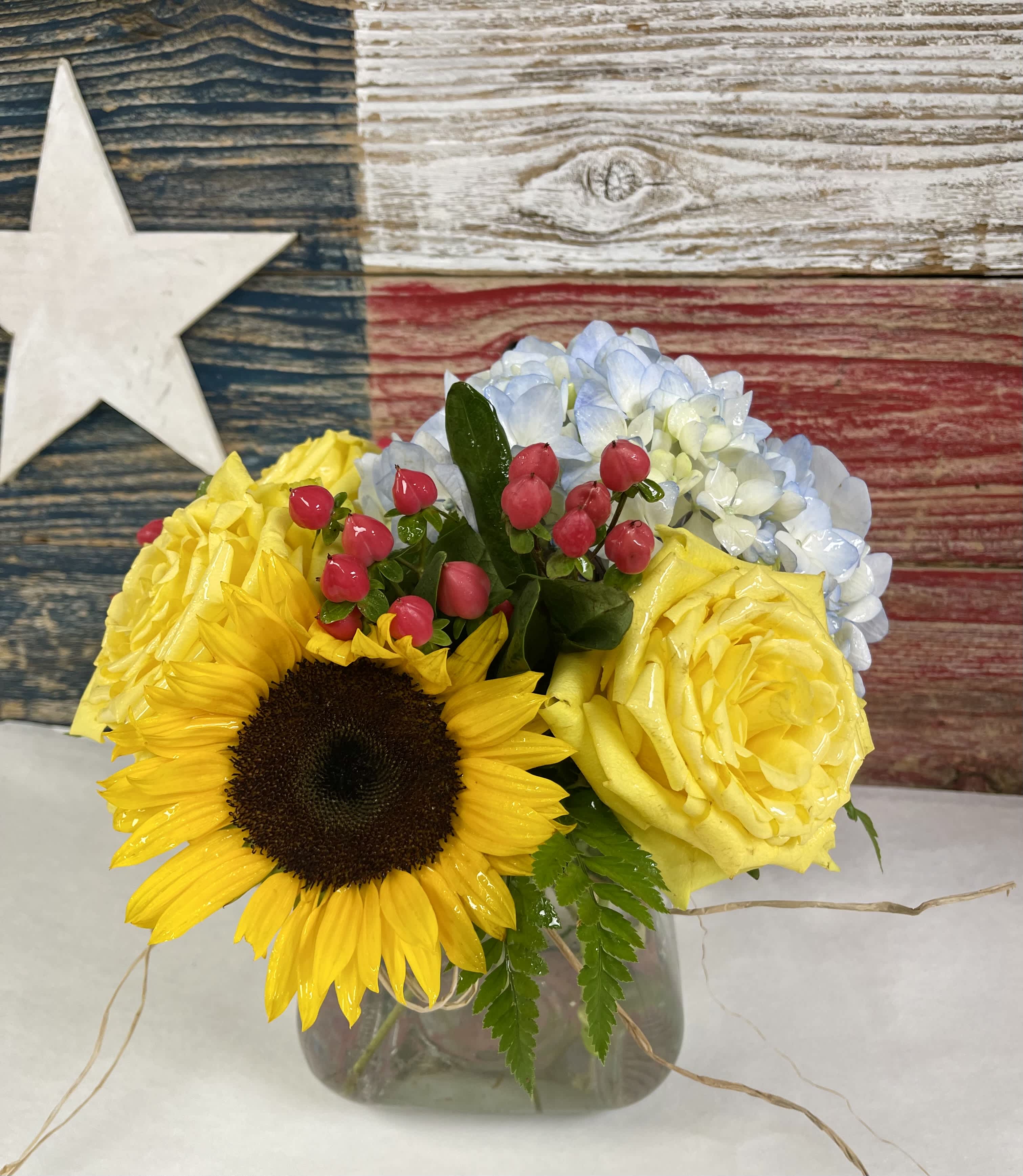 Bouquet of yellow roses, a sunflower, and blue hydrangeas in a glass vase