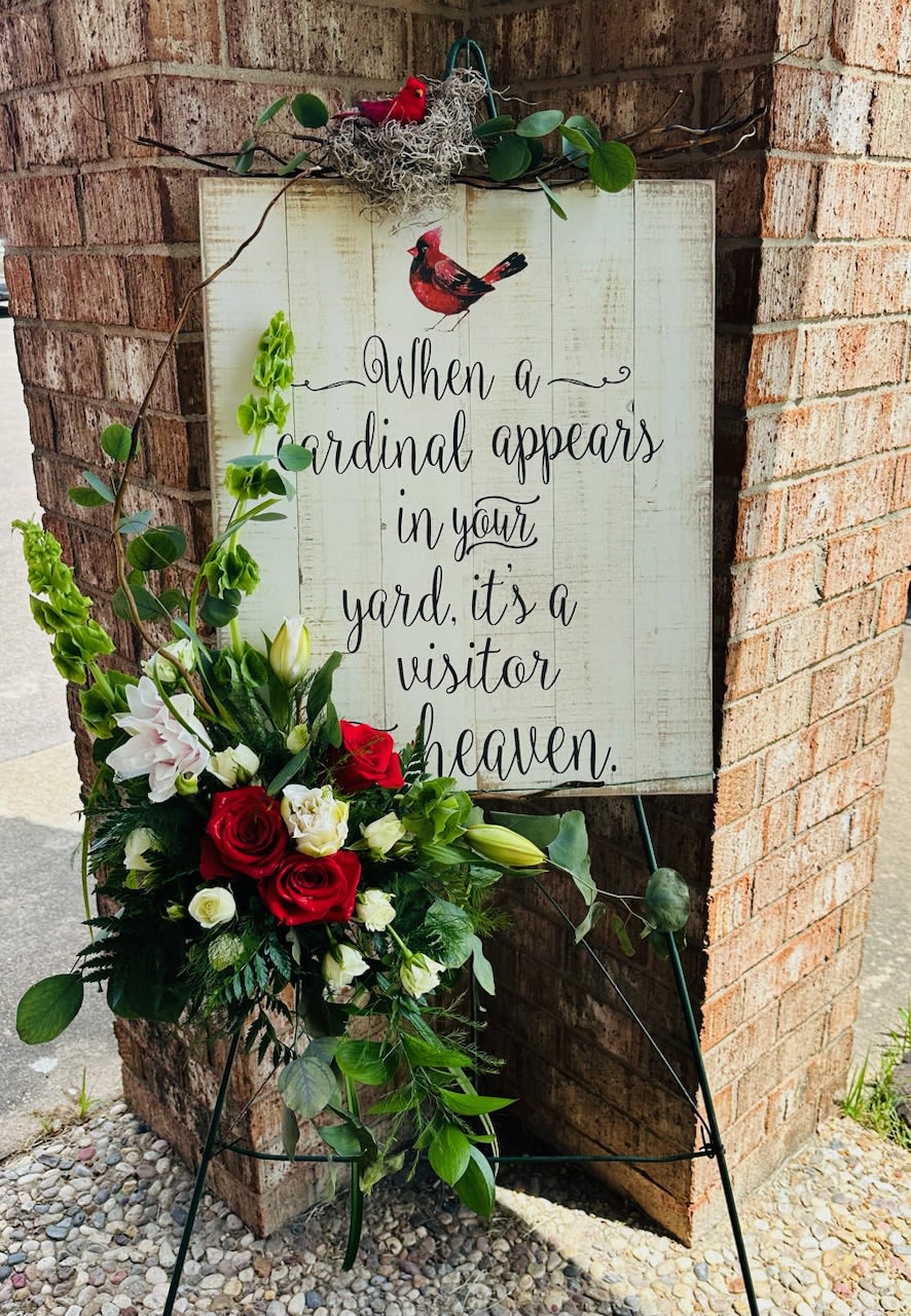 Standing floral easel with red, white, and green flowers beside a memorial sign