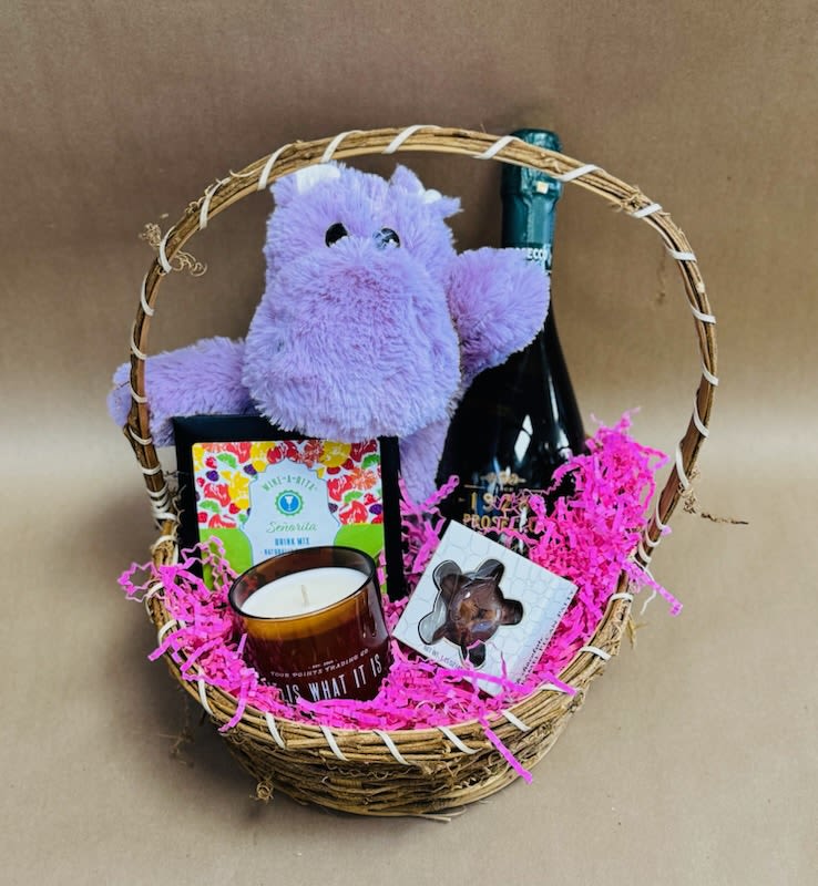 Gift basket with a plush purple hippo, candle, chocolate, and a bottle