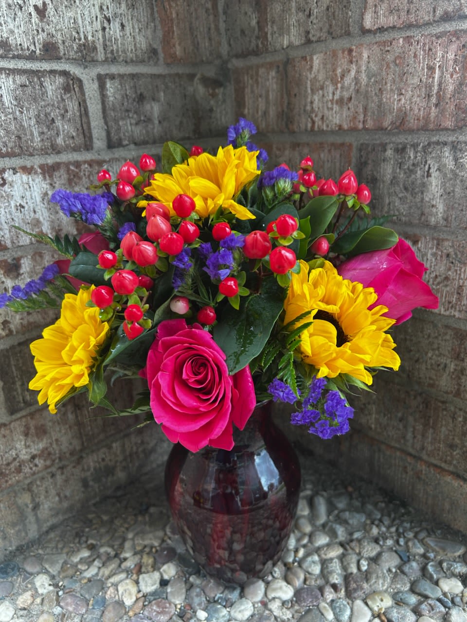 Bouquet of yellow sunflowers, pink roses, and red berries in a glass vase