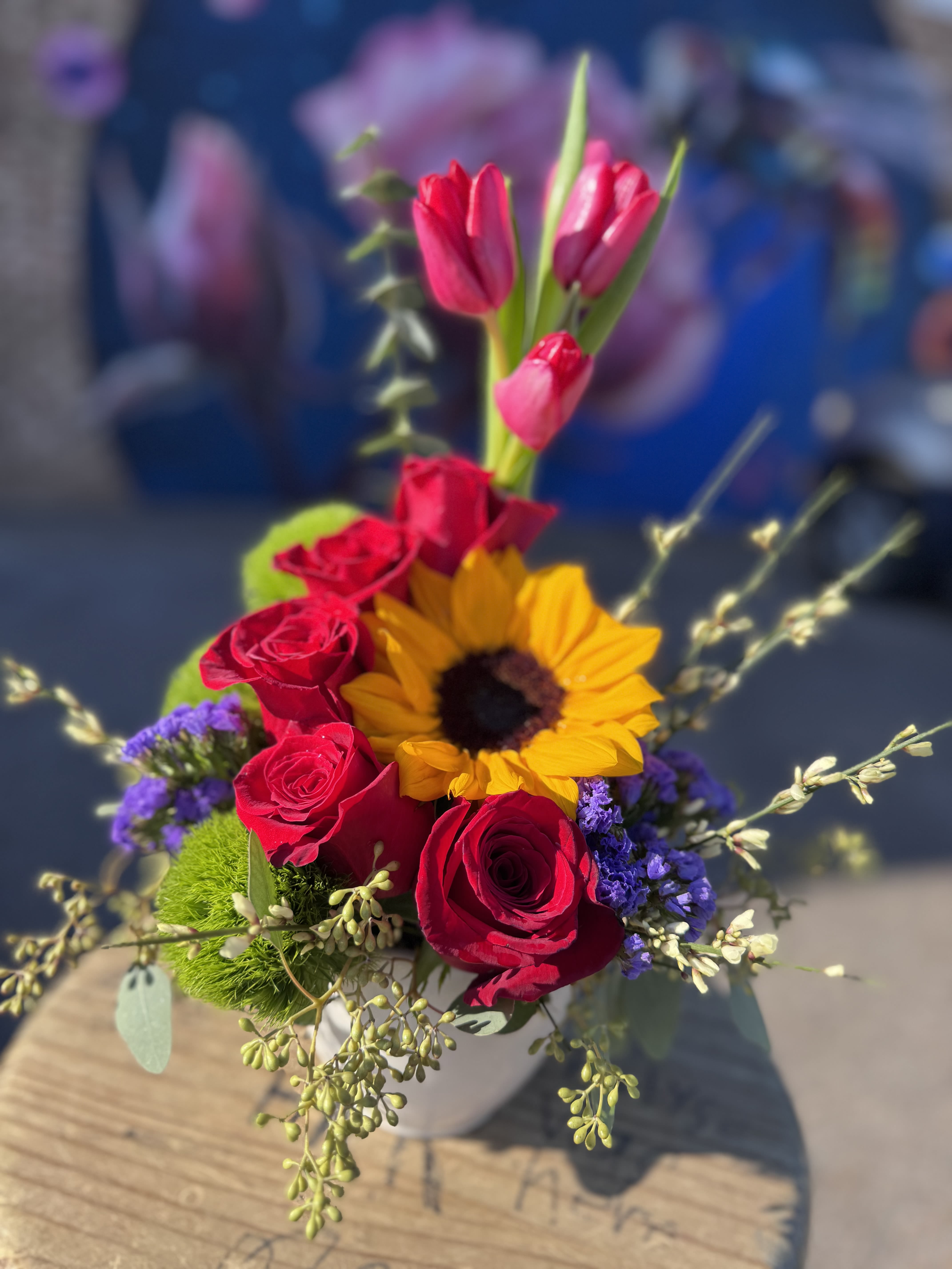Bouquet of red roses, pink tulips, and a sunflower in a white vase