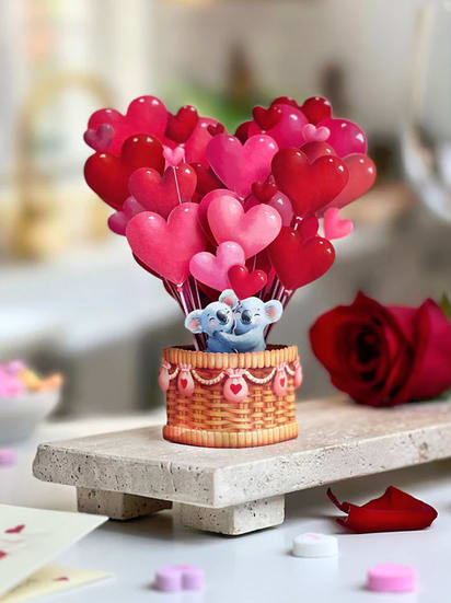 Add-on; Mini Heart Balloons Pop Up Card (Fresh Cut Paper) - Surprise your loved one with this adorable koala pop-up card! Taking off for adventure in their hot air balloon, this charming sentiment is sure to warm hearts. Perfect for Valentine’s Day, anniversaries, just because, or thinking of you, send some love with Mini Heart Balloons pop-up card!  Measures 6” high by 5” across. Printed on both sides.  This product is available as an add-on item but must be ordered in conjunction with any other product on our website to meet the $55 order minimum for delivery.  Please note that cancellations are subject to a 10% processing fee, or up to $25 for all refunds processed.