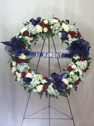 Heart-shaped funeral wreath with red, white, and blue flowers on an easel