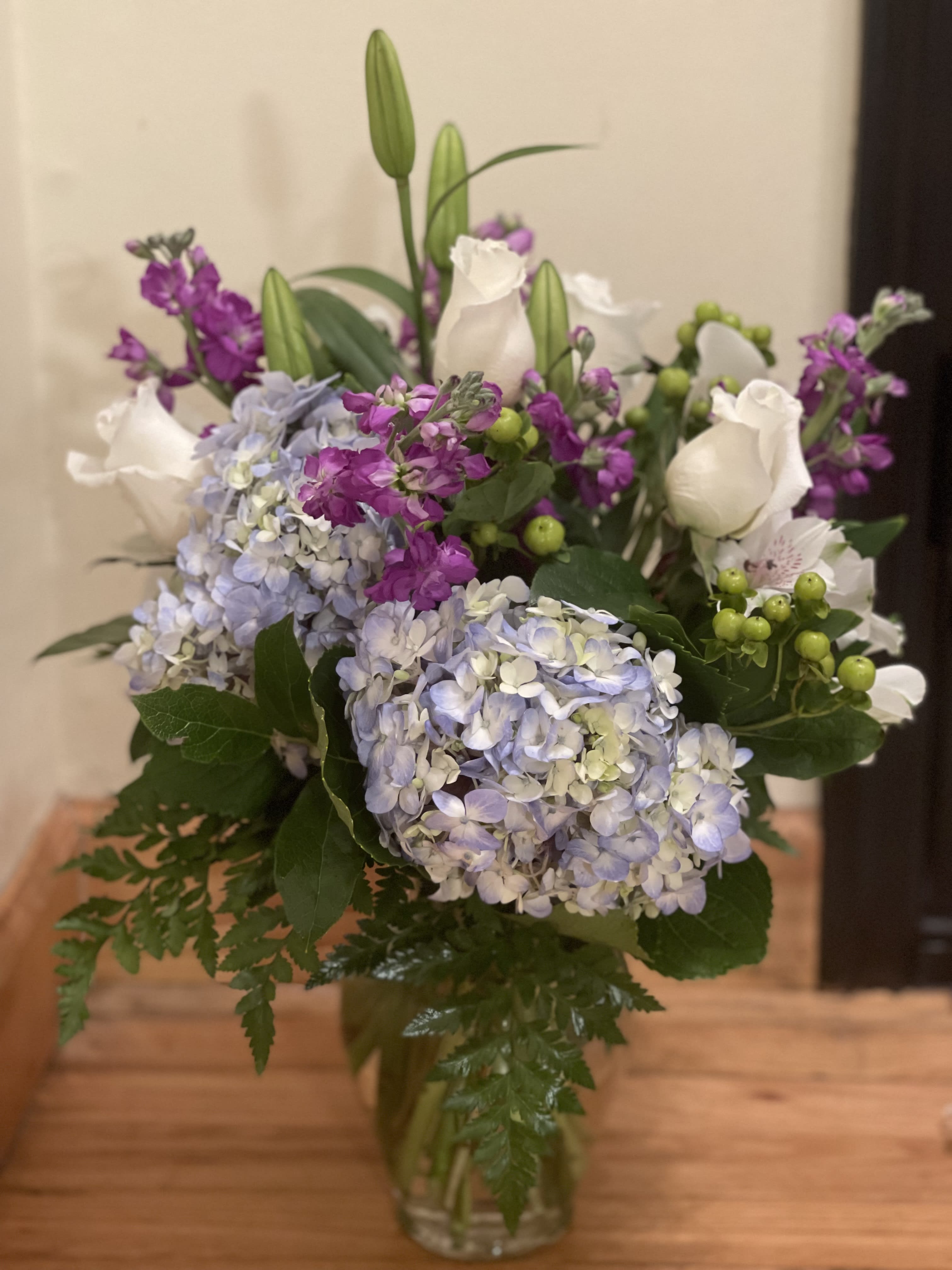 Bouquet of blue hydrangeas, white roses, and purple flowers in a glass vase