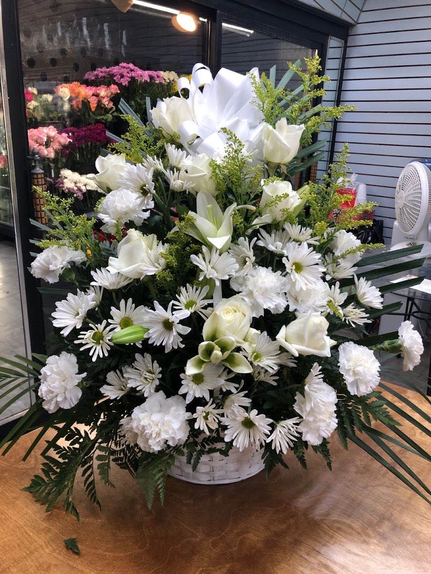 White floral arrangement in a white basket with daisies, roses, lilies, and carnations
