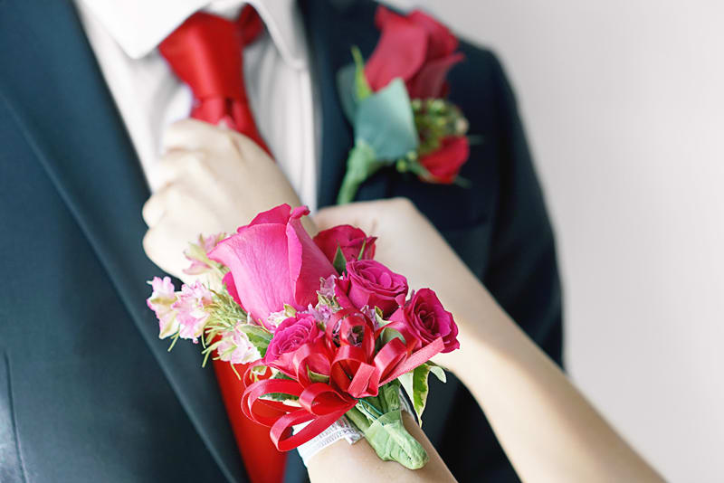 Pink rose corsage on a wrist with a matching boutonniere on a suit