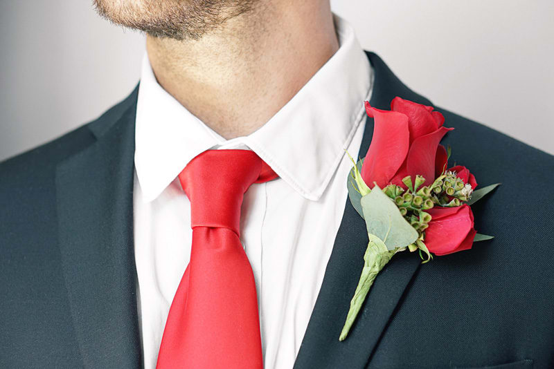 Red rose boutonniere on a suit lapel with a red tie