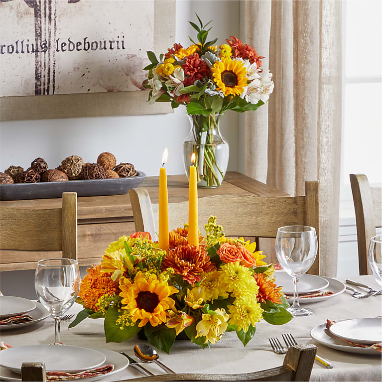 Yellow and orange floral centerpiece with two candles on a dining table