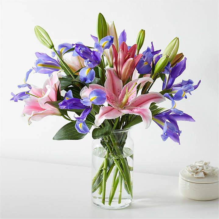 Bouquet of pink lilies and purple irises in a clear glass vase