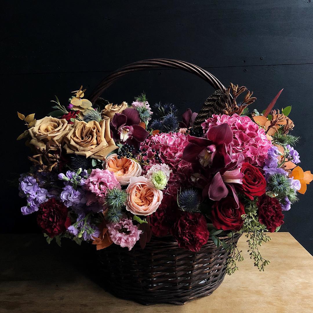 Basket arrangement of roses, orchids, and hydrangeas in deep pink and burgundy tones