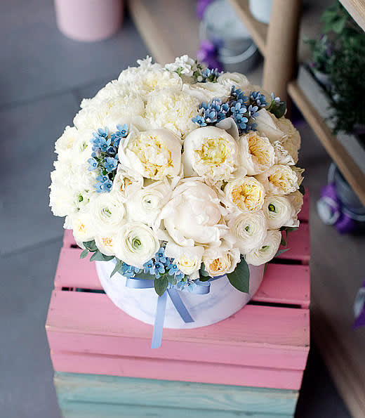 Round bouquet of white flowers with small blue accents in a white box