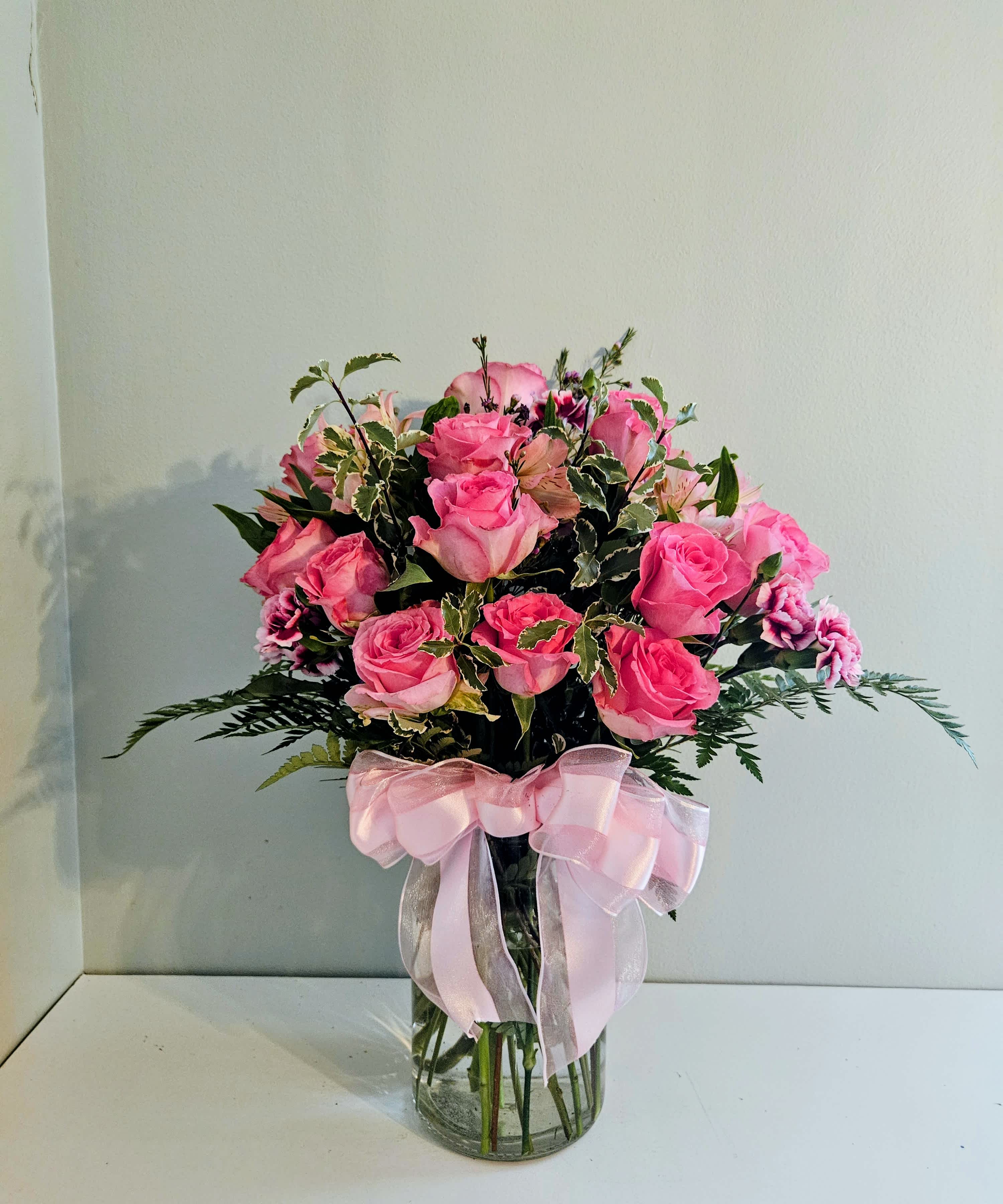 Pink roses arranged in a clear glass vase with a pink ribbon