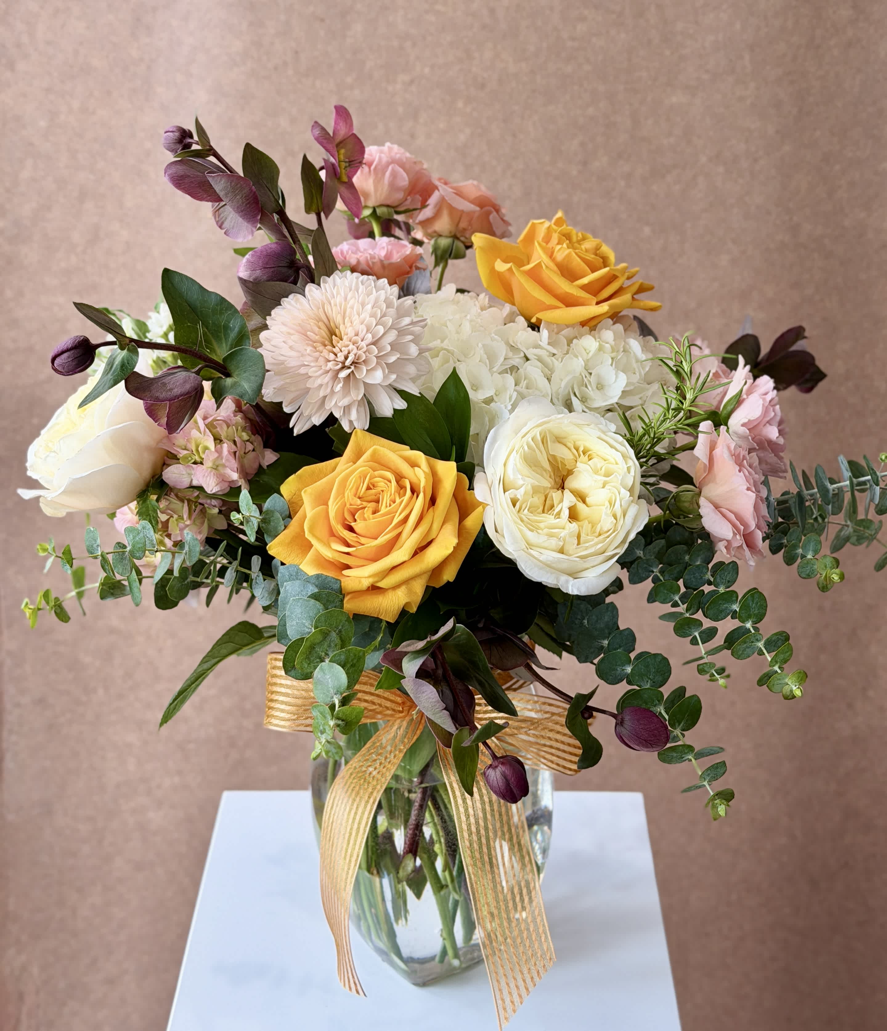 Bouquet of yellow, white, pink, and purple flowers in a glass vase with a ribbon