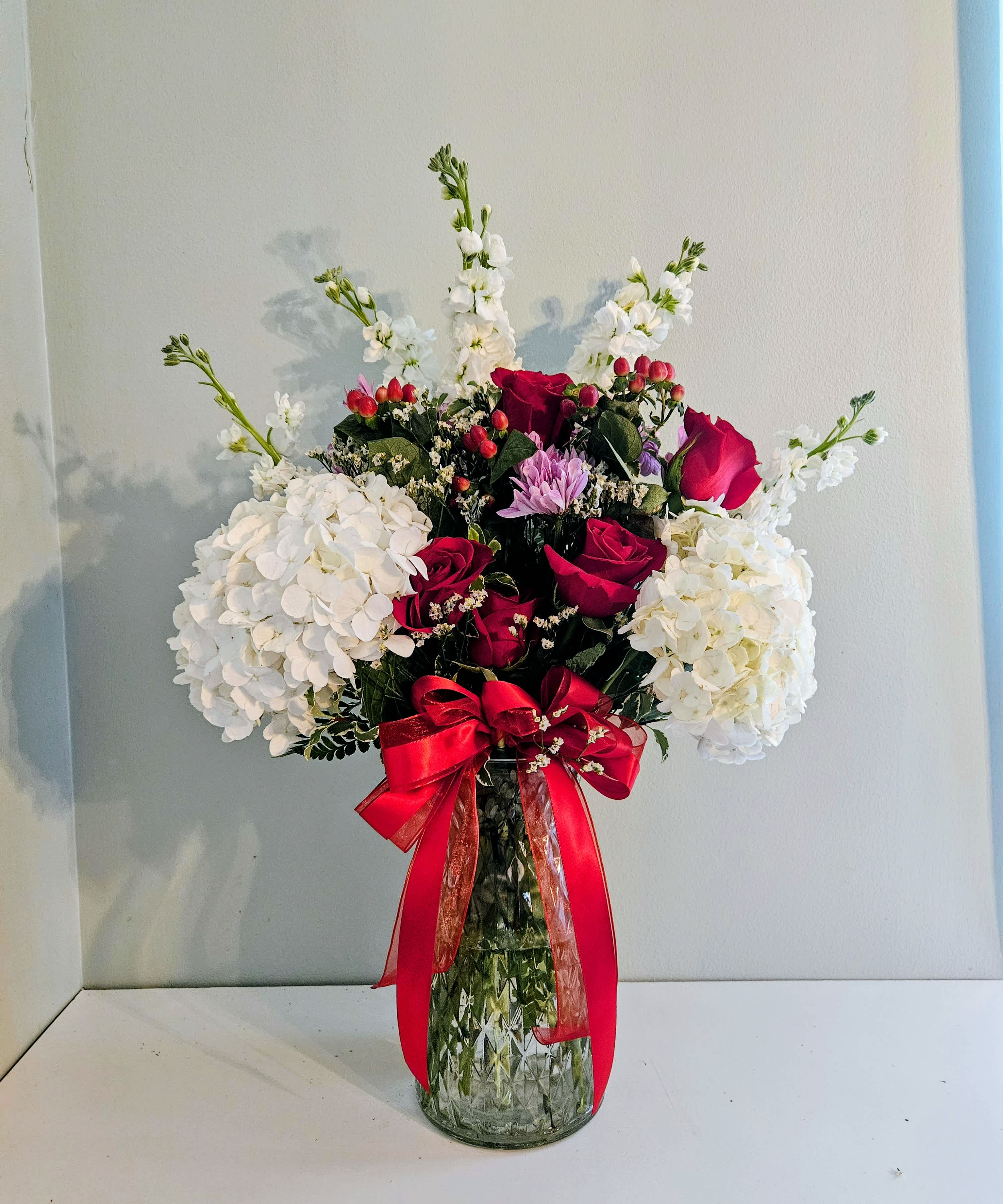 Red roses and white hydrangeas in a clear glass vase with a red ribbon