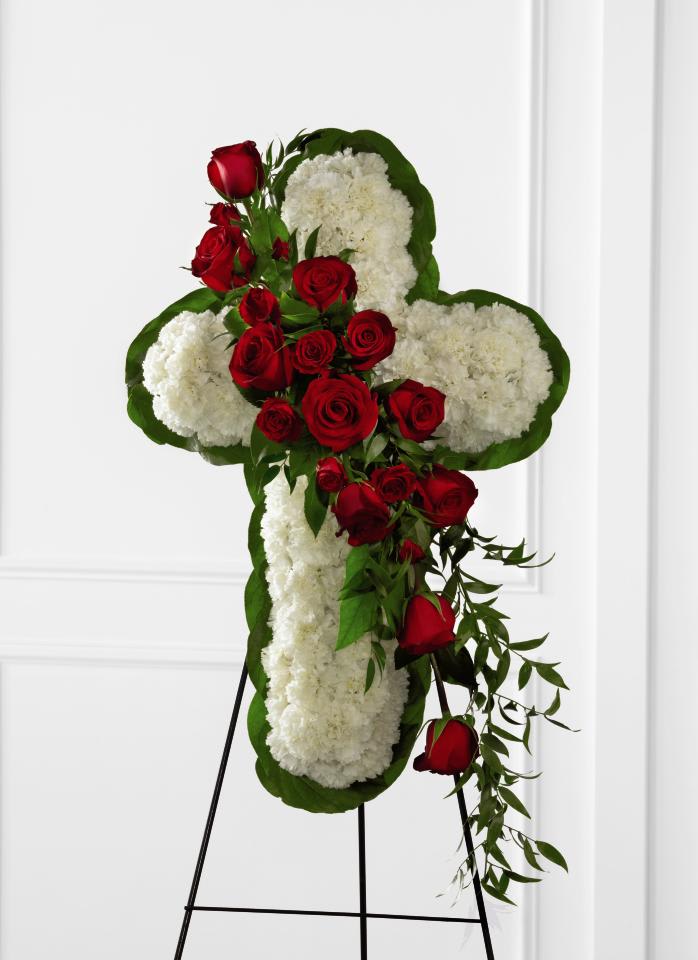Cross-shaped floral tribute with red roses and white flowers on an easel