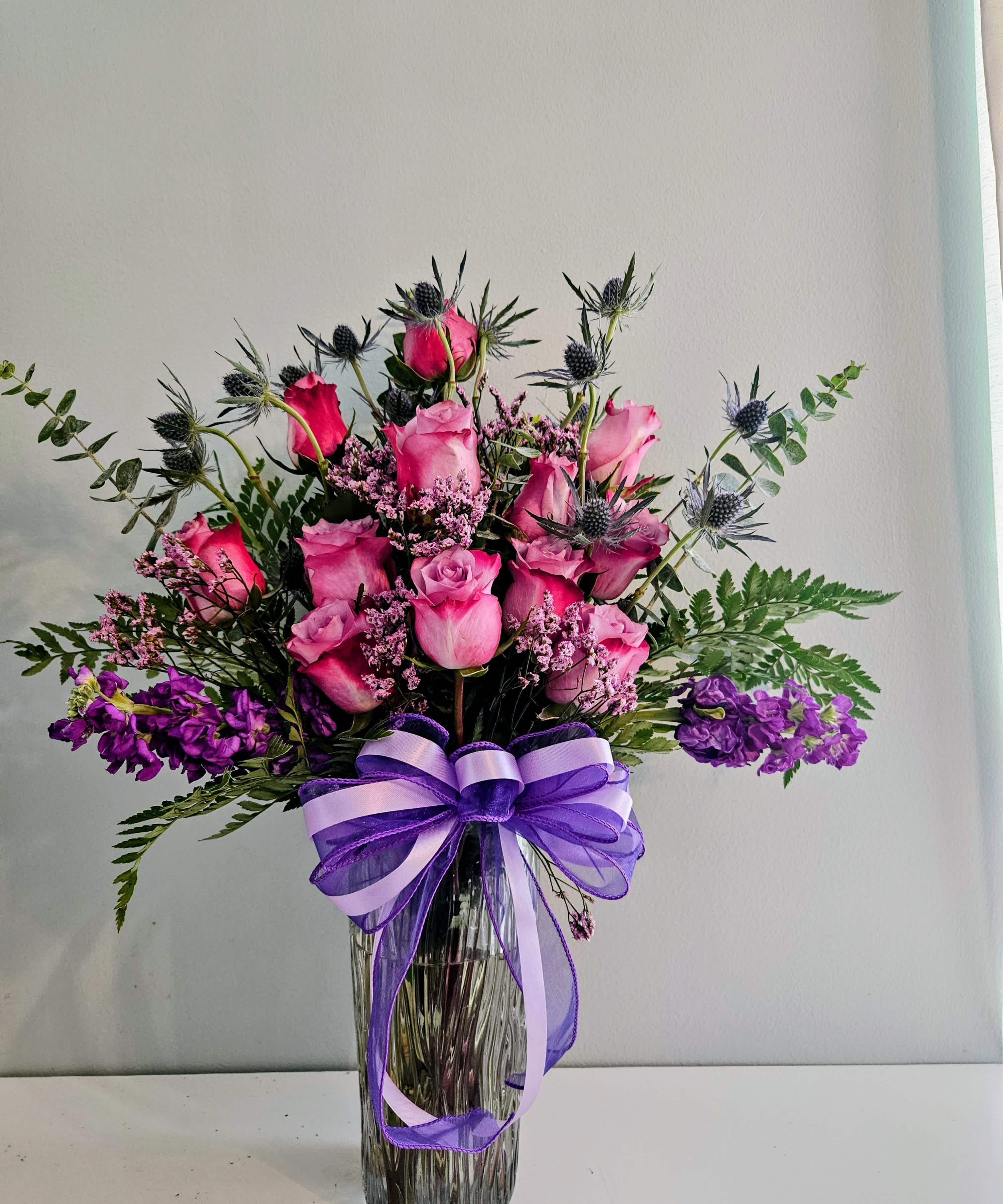 Pink and purple rose bouquet in a clear glass vase with a purple ribbon