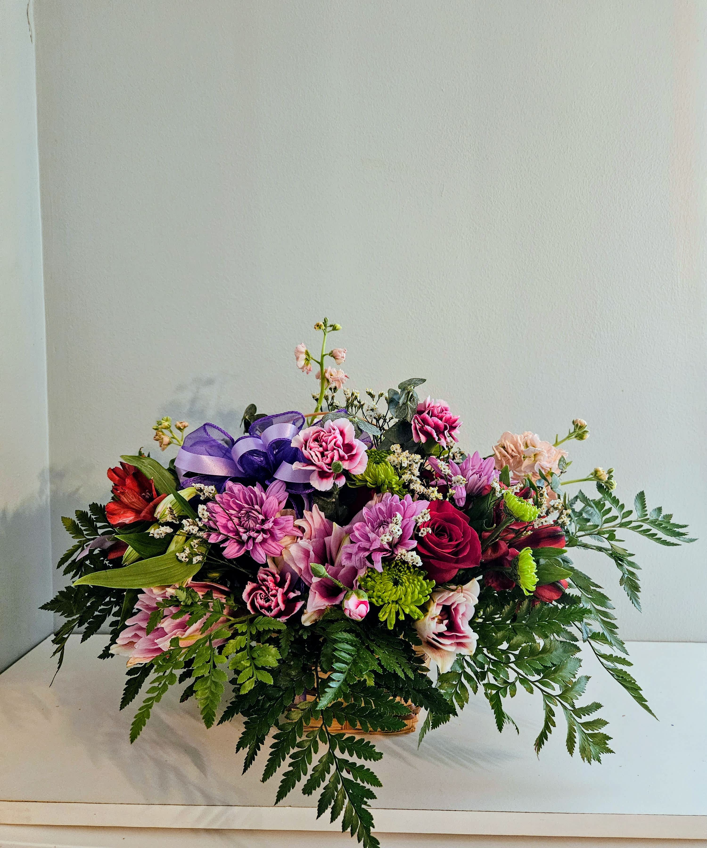 Mixed bouquet of pink and purple flowers in a basket with a purple ribbon