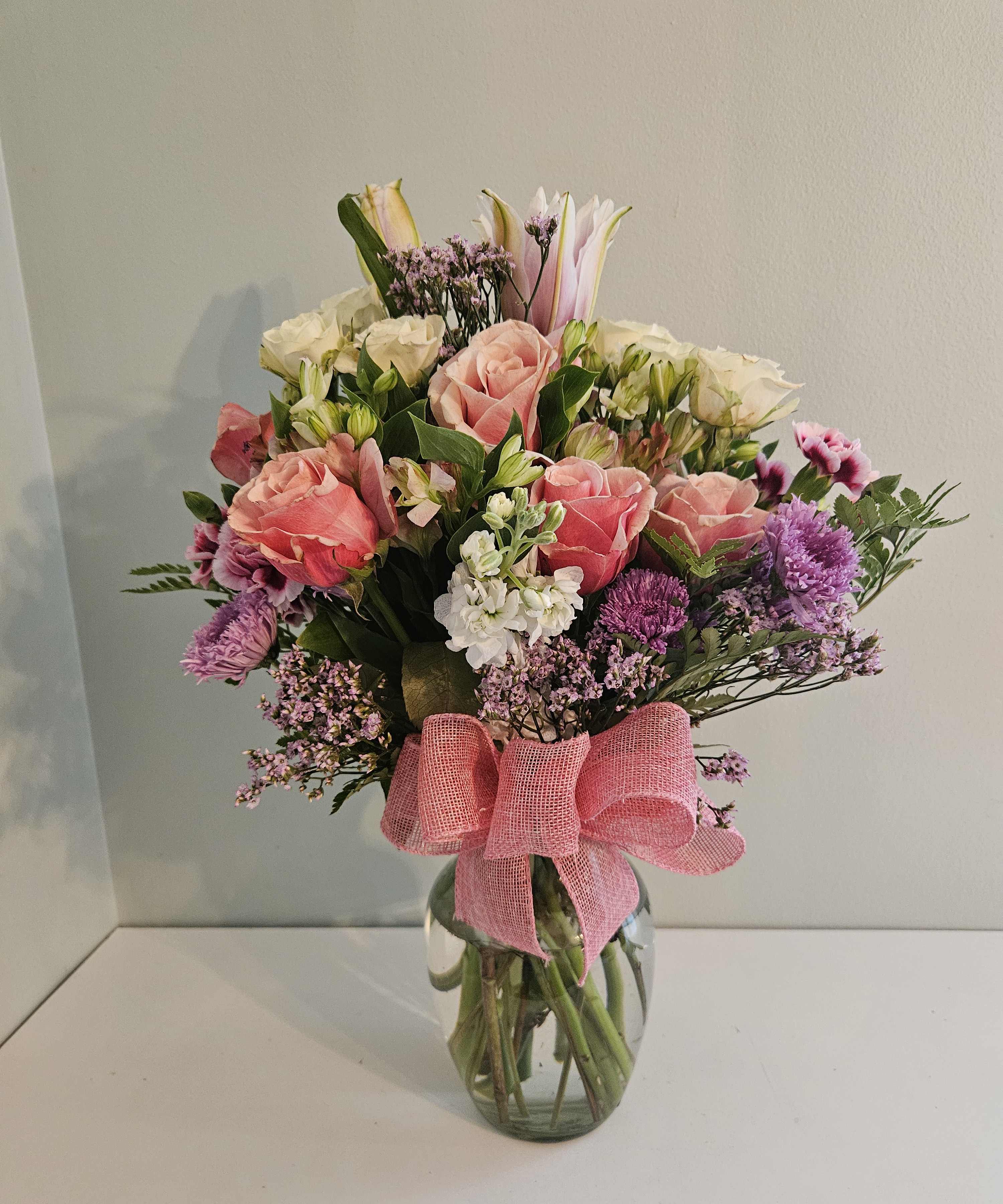 Mixed bouquet of pink and white flowers in a glass vase with a pink ribbon