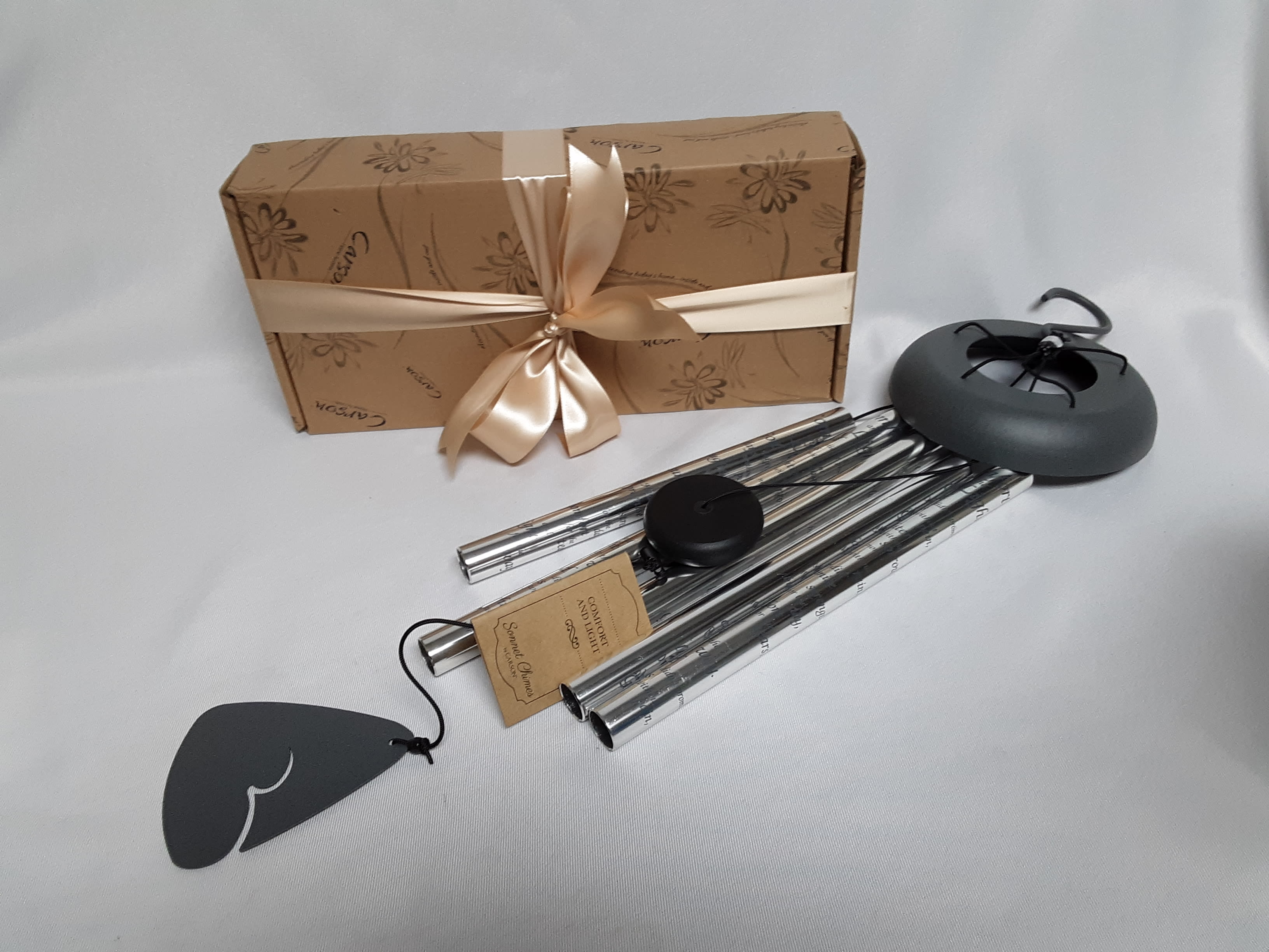 Gift box with ribbon and metal wind chimes on a white surface