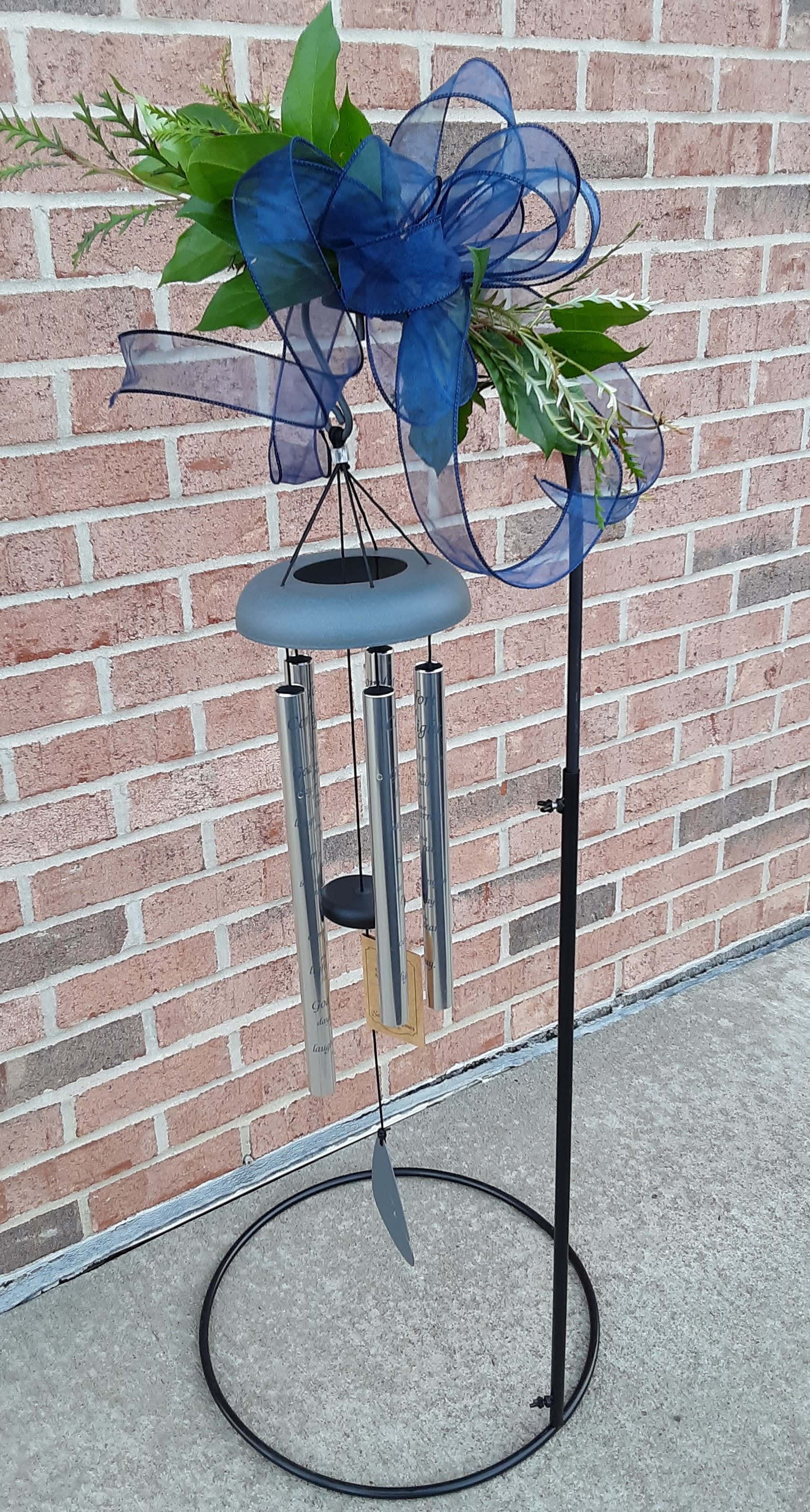 Wind chime with blue ribbon and greenery on a black metal stand