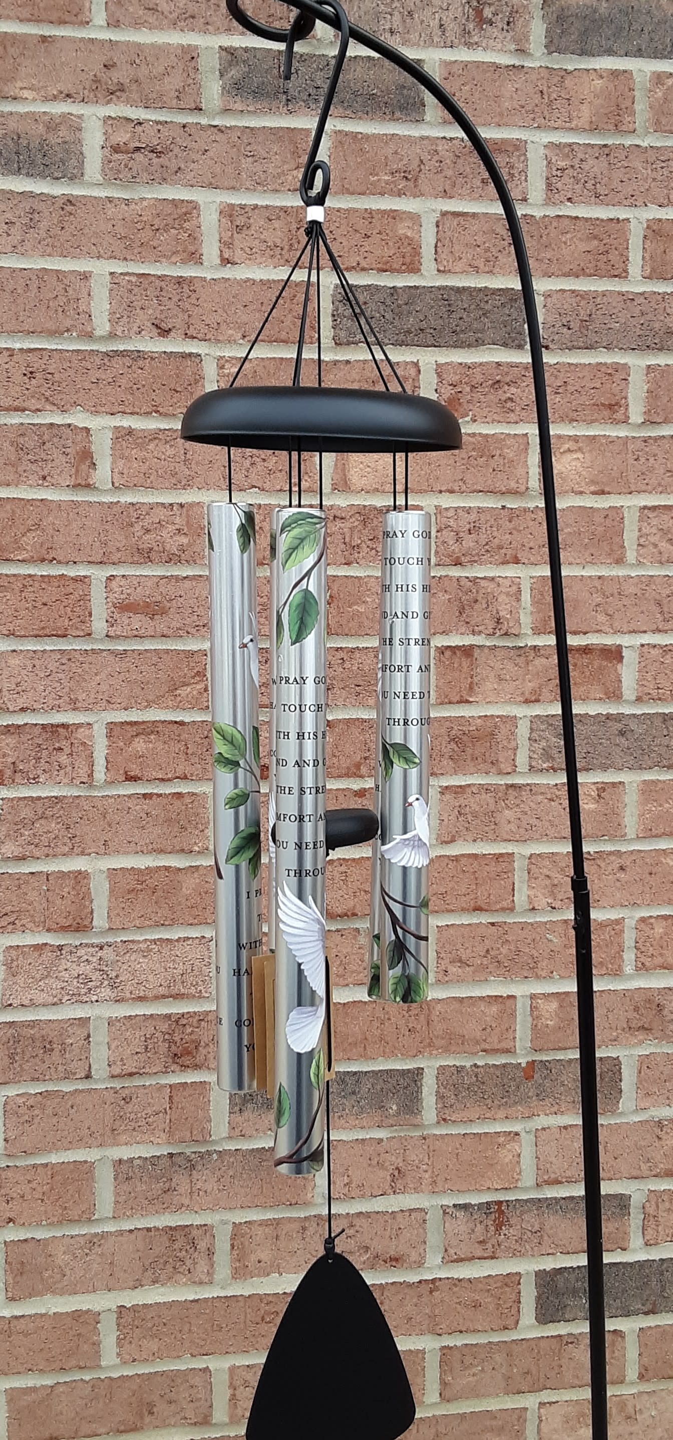 Black metal wind chime with silver tubes and bird designs hanging on a brick wall.