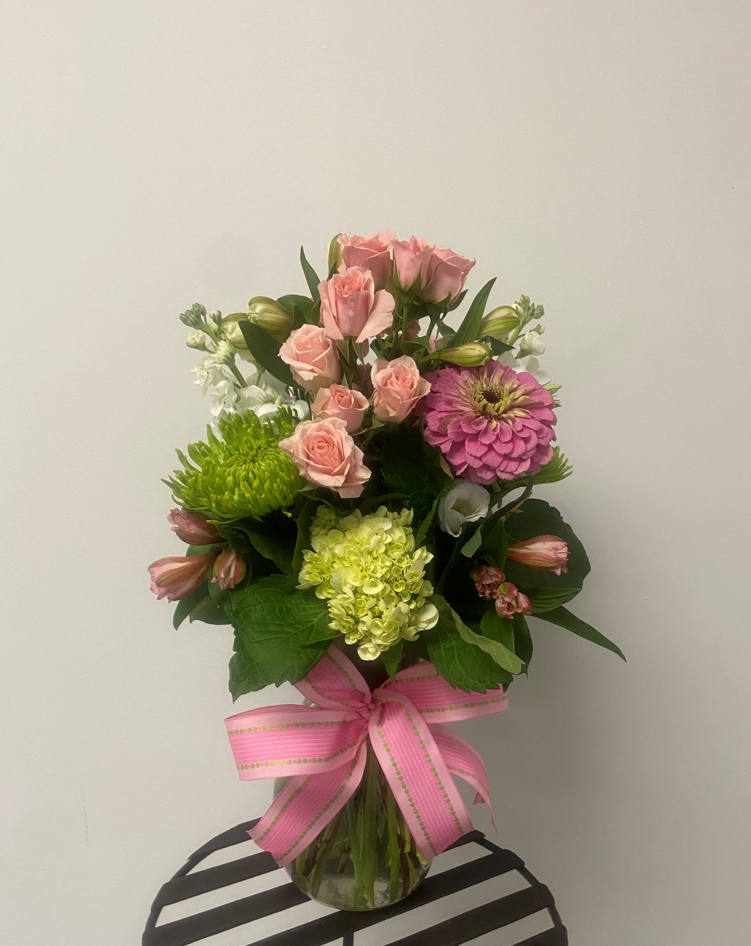 Pink roses and mixed blooms in a glass vase with a pink ribbon
