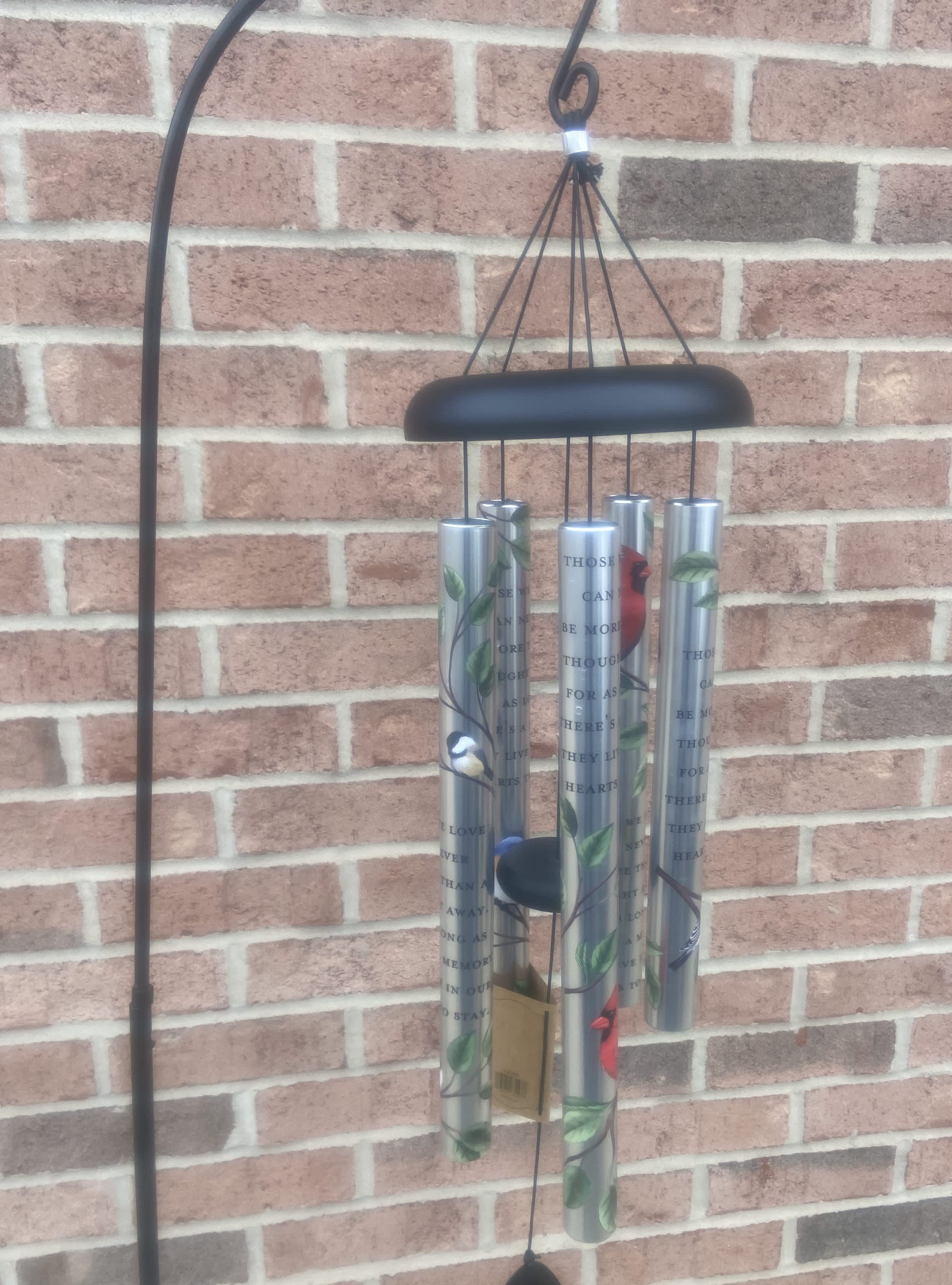 Black metal wind chime with silver tubes hanging against a brick wall