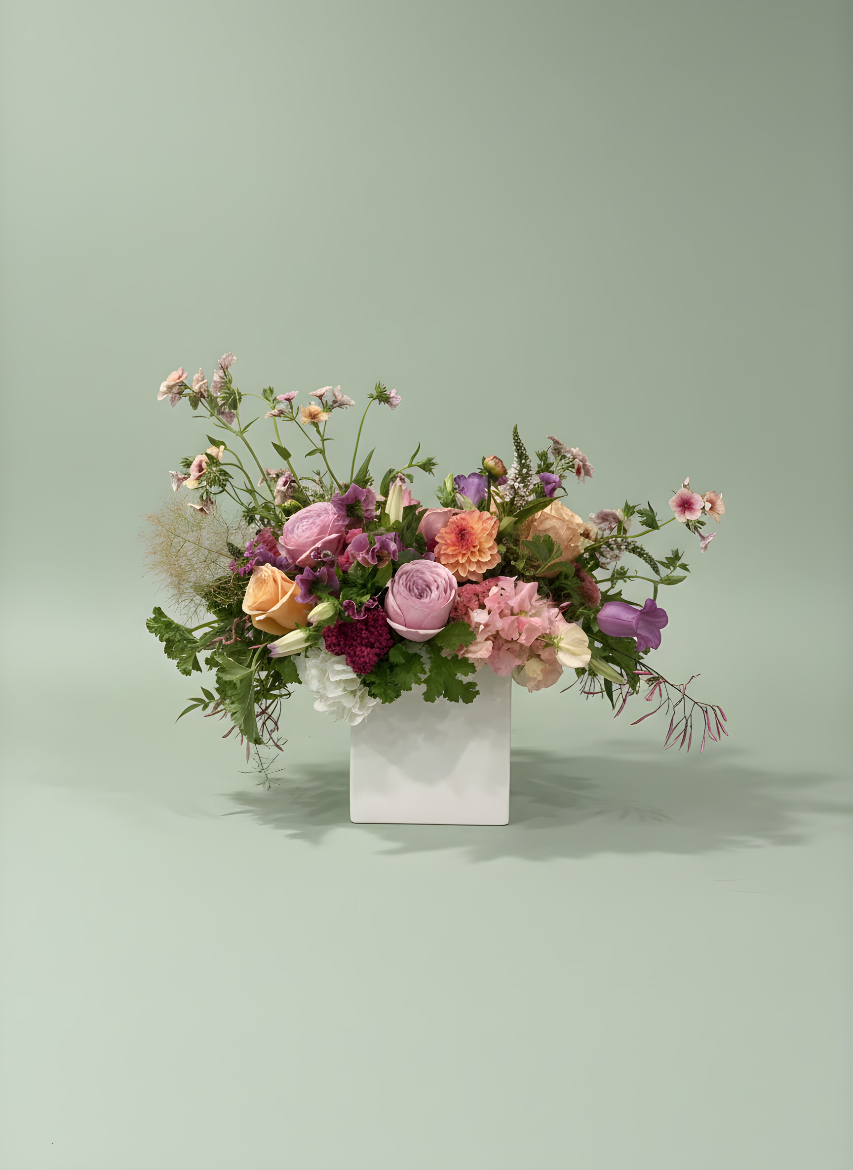 Mixed pink, peach, and purple flowers in a white vase