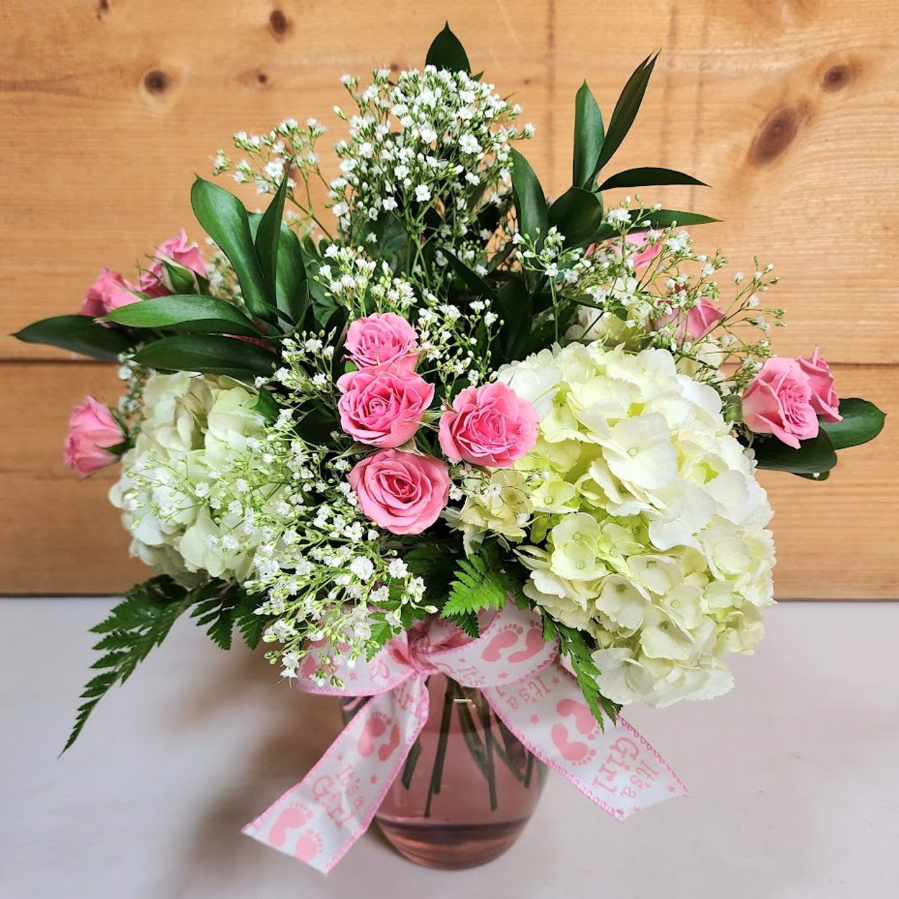 Pink roses and white hydrangeas in a glass vase with a pink ribbon