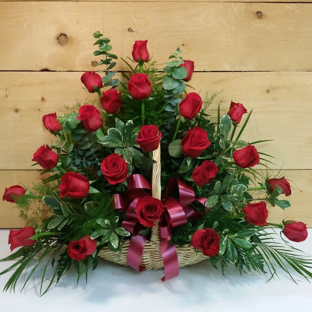 Basket arrangement of red roses with greenery and a burgundy ribbon