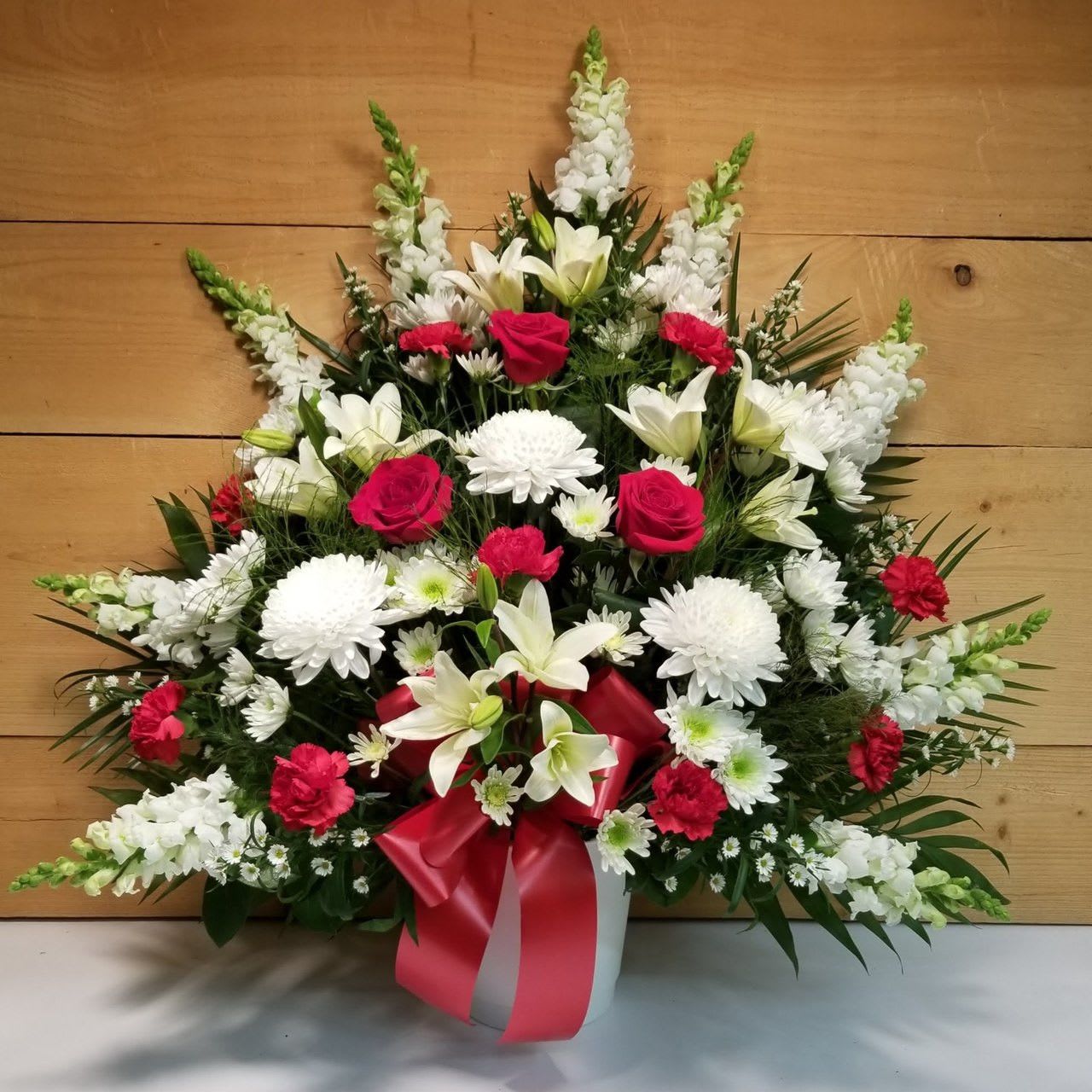 White and red floral arrangement in a vase with a pink ribbon
