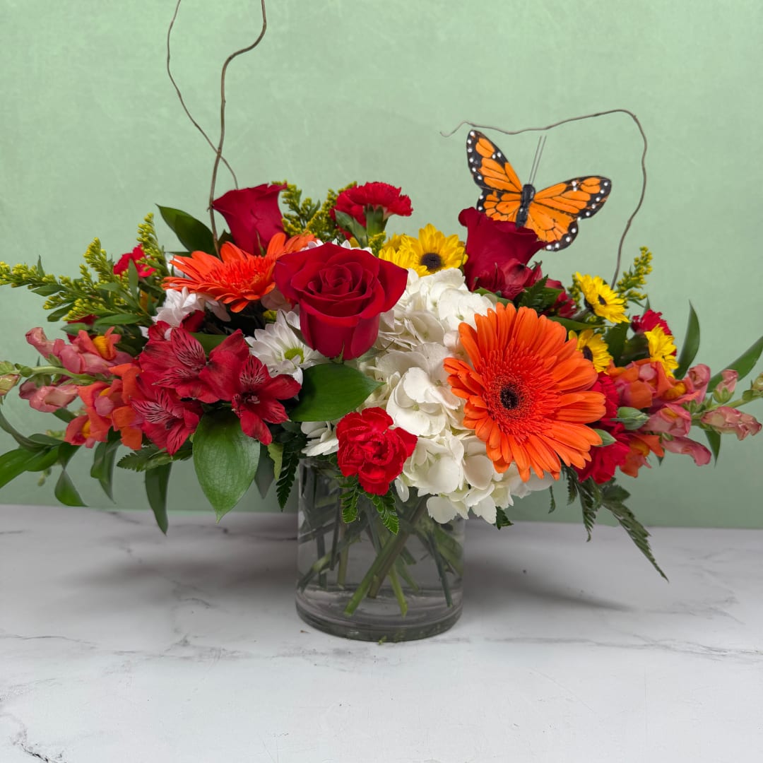 Mixed bouquet of red, orange, white, and yellow flowers in a glass vase