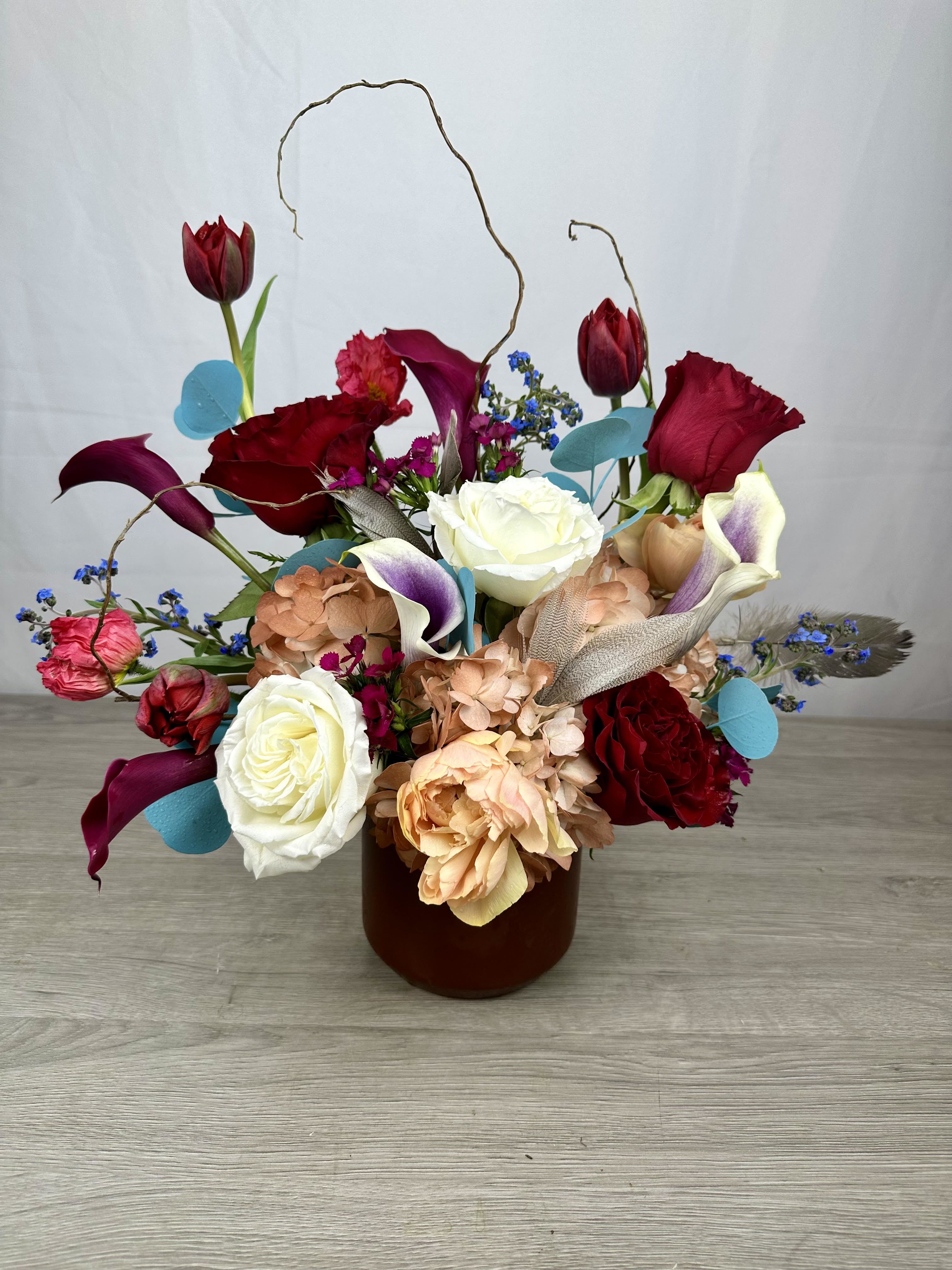 Wine &amp; Wildflowers - This arrangement has a romantic, artistic feel with rich burgundy blooms, creamy whites, soft peach hydrangeas, elegant calla lilies, and whimsical curly willow.