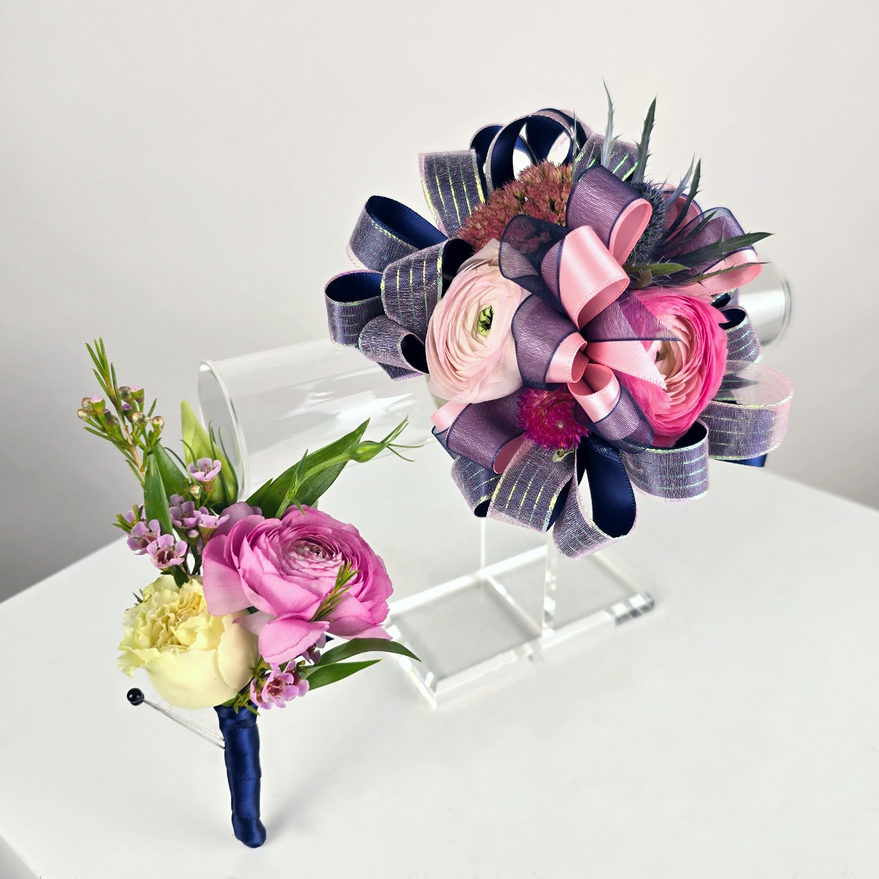 Two floral boutonnieres with pink and cream blooms and ribbon accents
